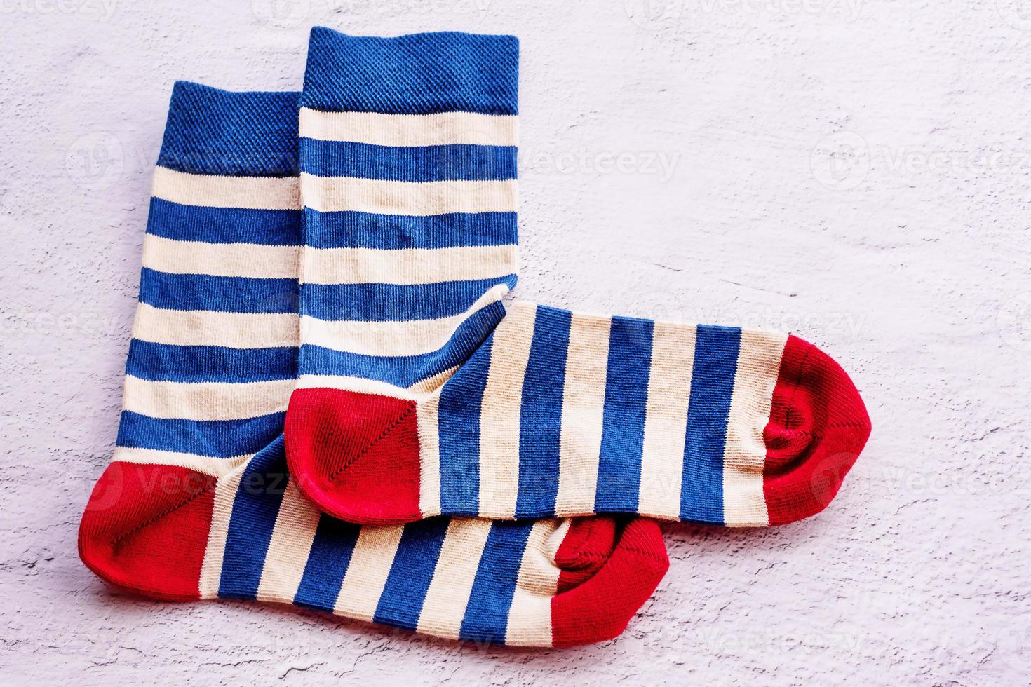 A pair of socks on a gray cement background. Blue and beige striped socks with a red toe and heel. photo
