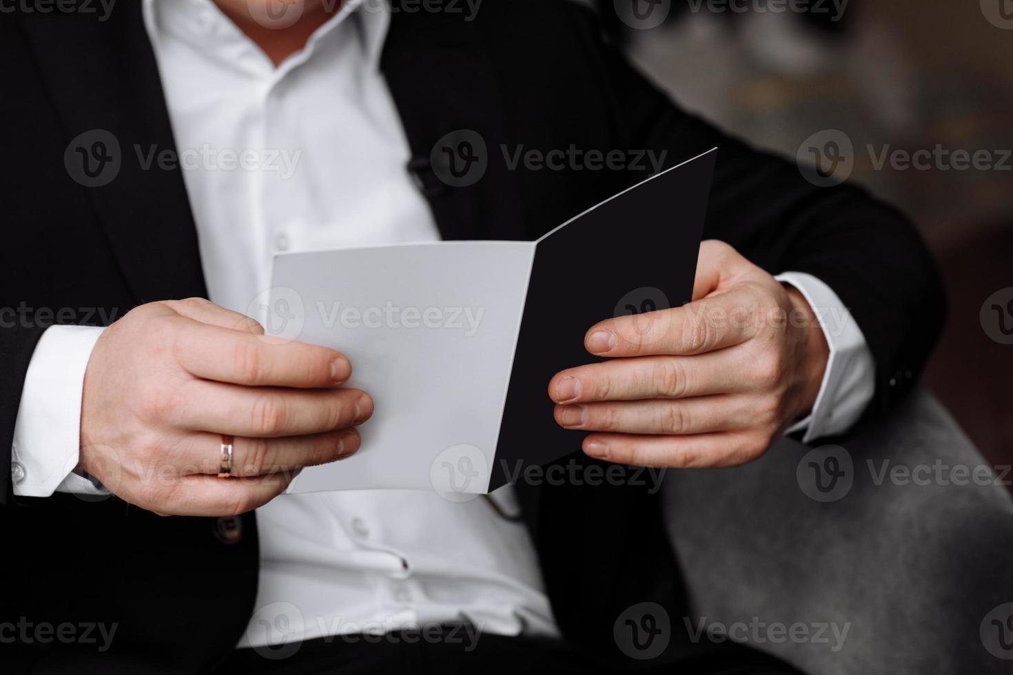 the groom holds an envelope with a letter from the bride. man is reading and sitting in the chair near the window. A letter for the groom. declaration of love. photo