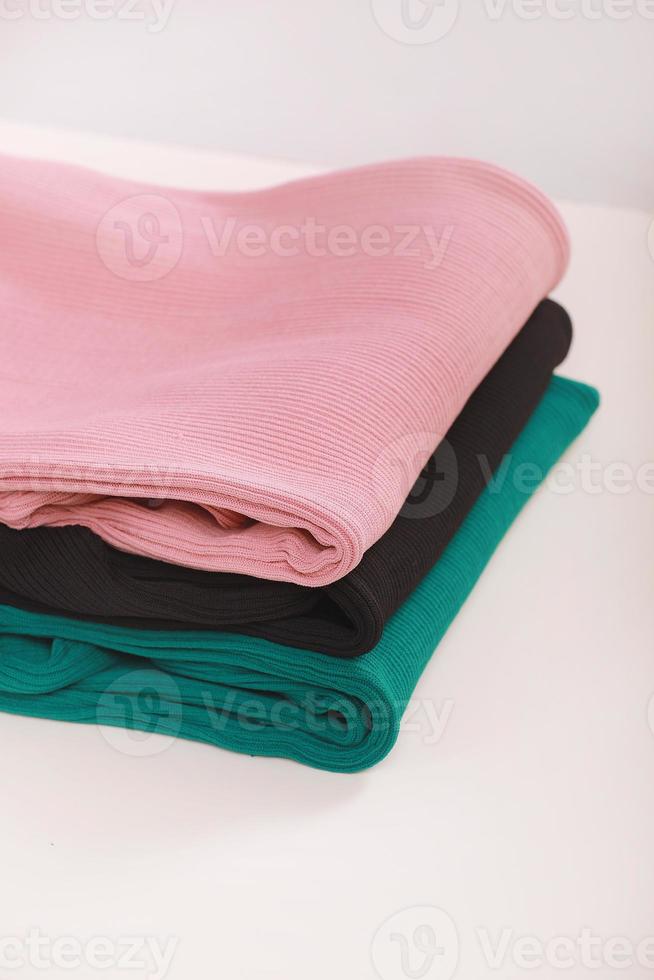 Pile of knitted warm colorfull sweaters with different knitting patterns folded in stack on white background, white wall background. Fall winter season knitwear. Close up, copy space for text photo