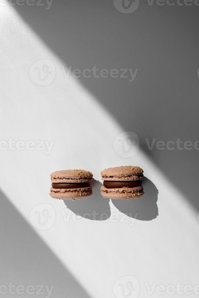 two sweet brown chocolate french macaroons or macarons dessert isolated on white background with light rays from window. copy space. photo