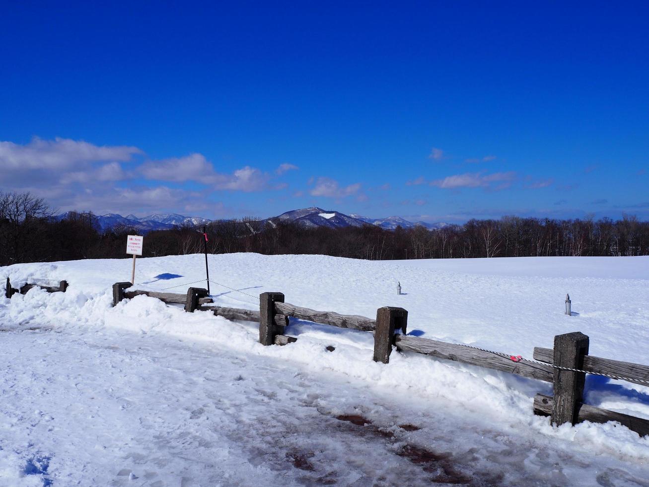 Wooden fence separates the area of the snow. Bright sunlight reflects on the white snow. photo