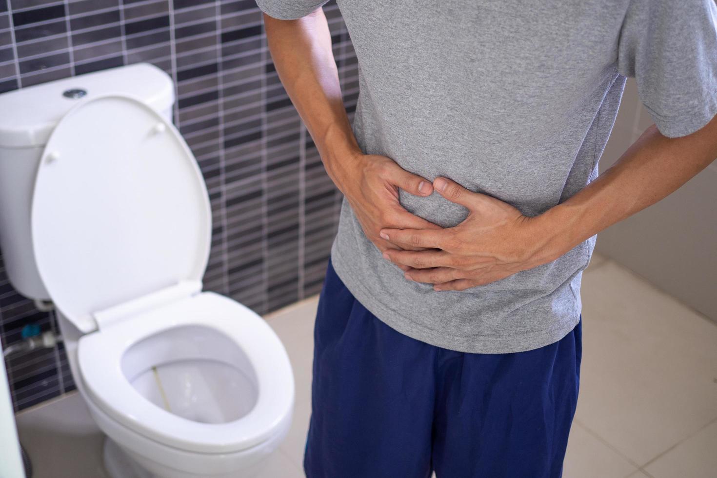 los hombres tienen dolor de estómago y usan sus manos para sostener su estómago en el baño. estreñimiento o cáncer de colon foto