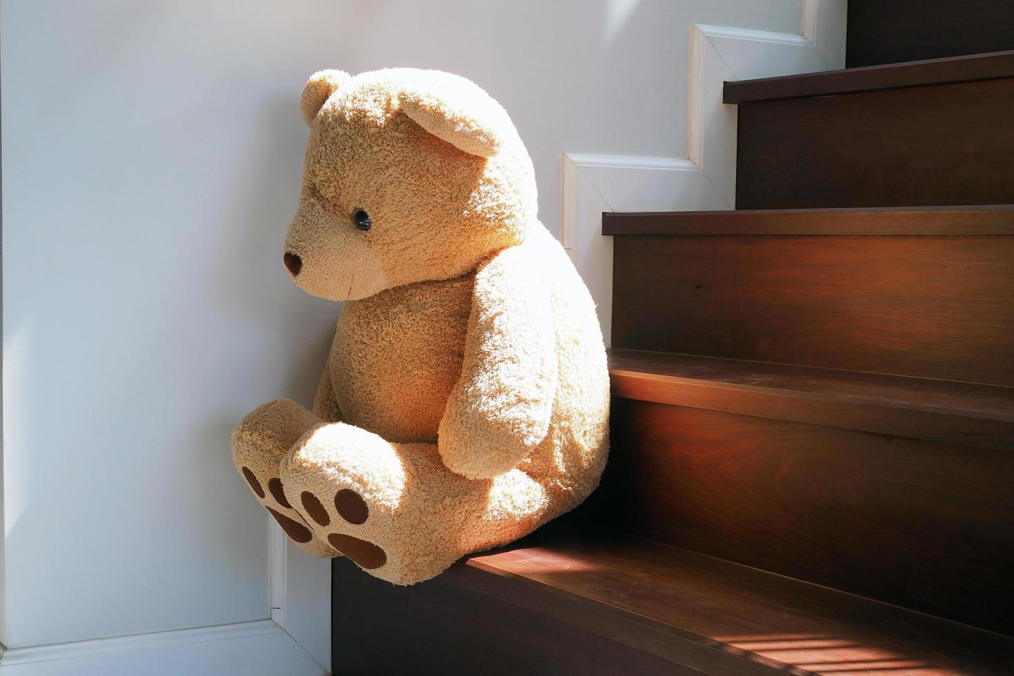 Child concept of sorrow. Teddy bear sitting leaning against the wall of the house alone, look sad and disappointed. photo