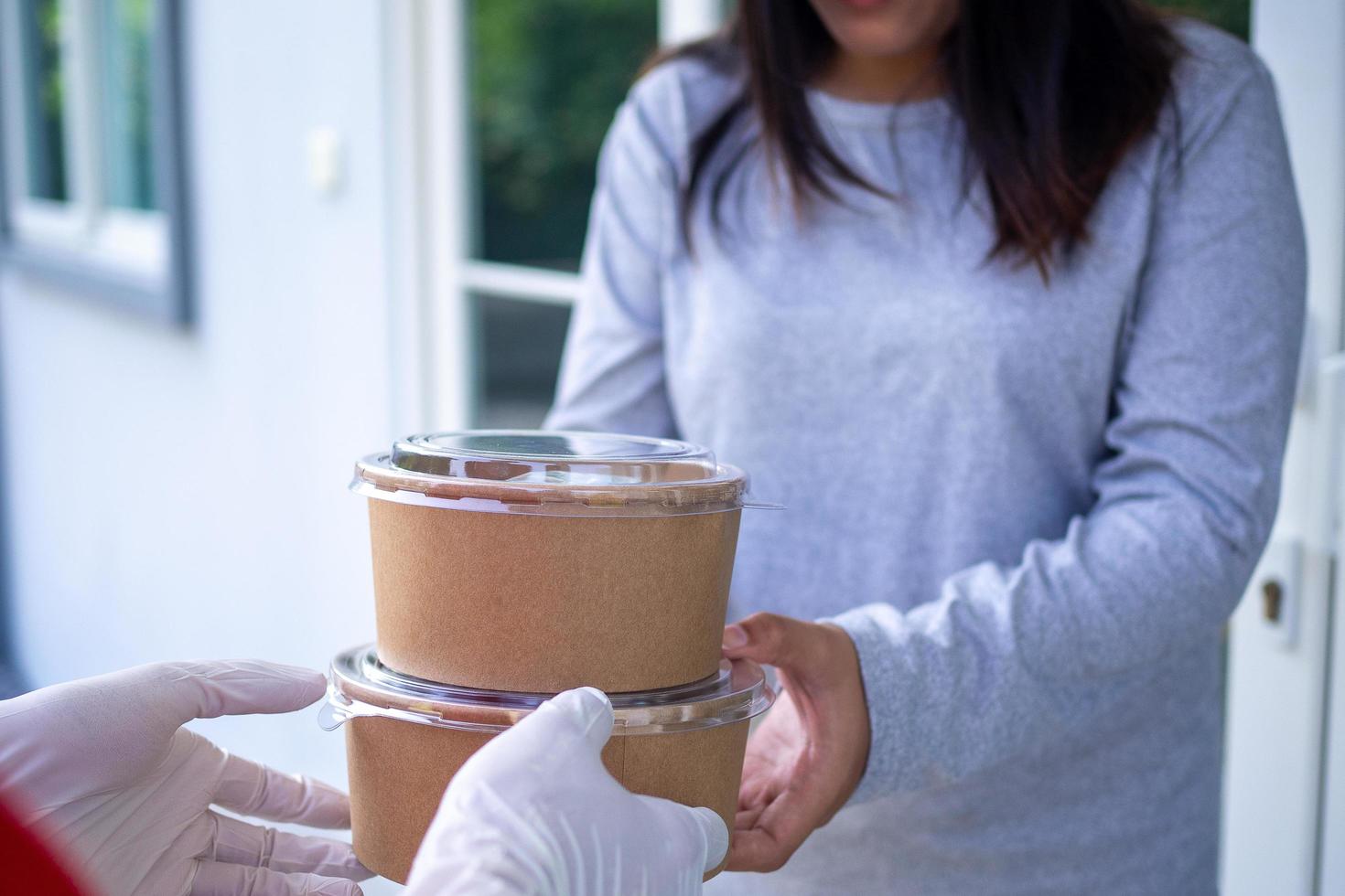 Delivery staff wear gloves for good hygiene, send food boxes to recipients in front of the house. Order food online and fast delivery. photo