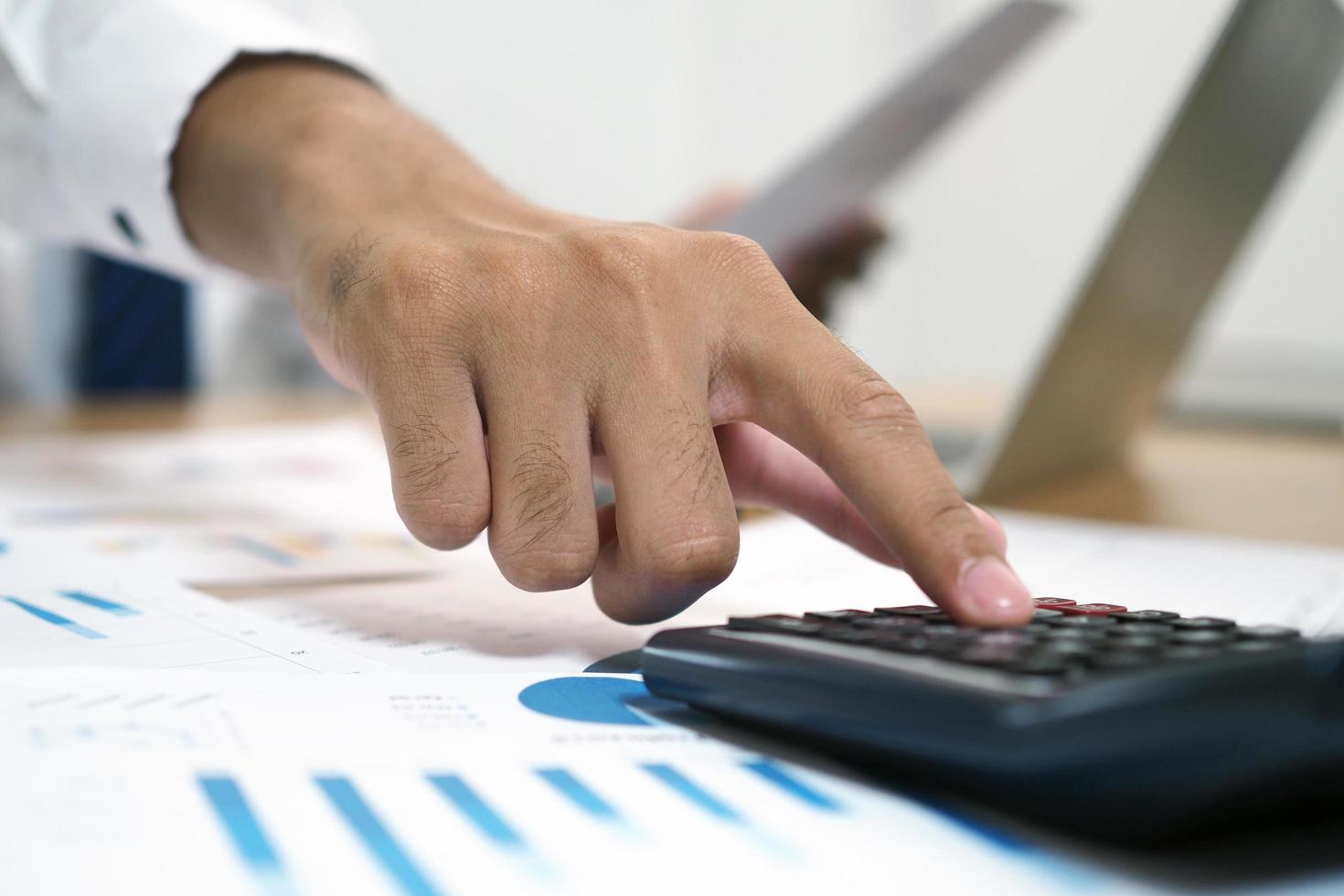 Close-up pictures of businessmen are pressing the calculator to calculate business information. Documents and graphs about accounting are on the table. photo