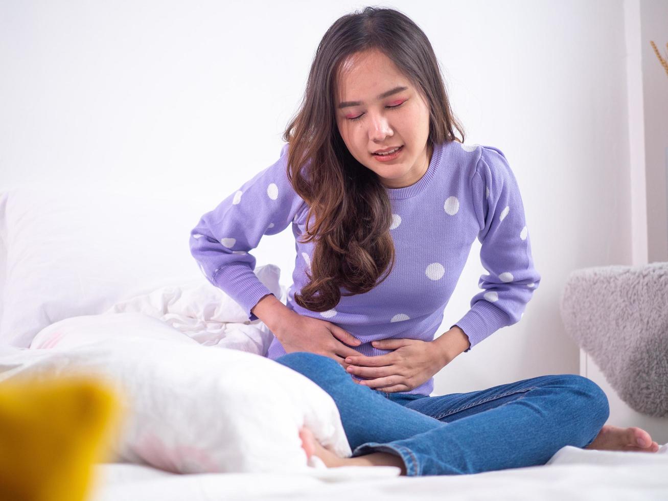 mujeres asiáticas con menstruación y calambres menstruales. una niña sentada con dolor en una cama en casa. foto