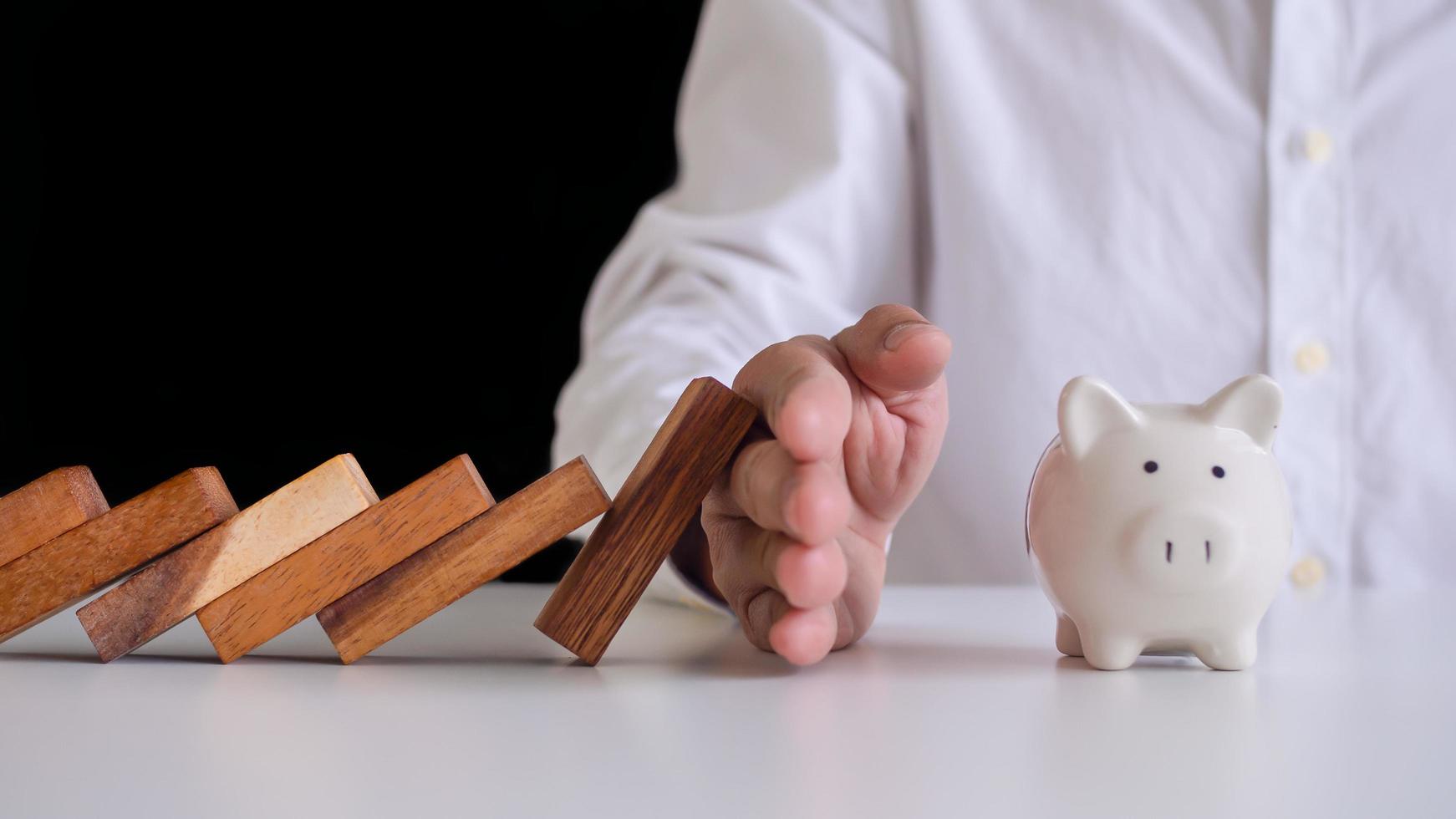 Insurance agents or family leaders are using hands to prevent domino from falling into the piggy bank . Prevention of external hazards. money insurance plan photo