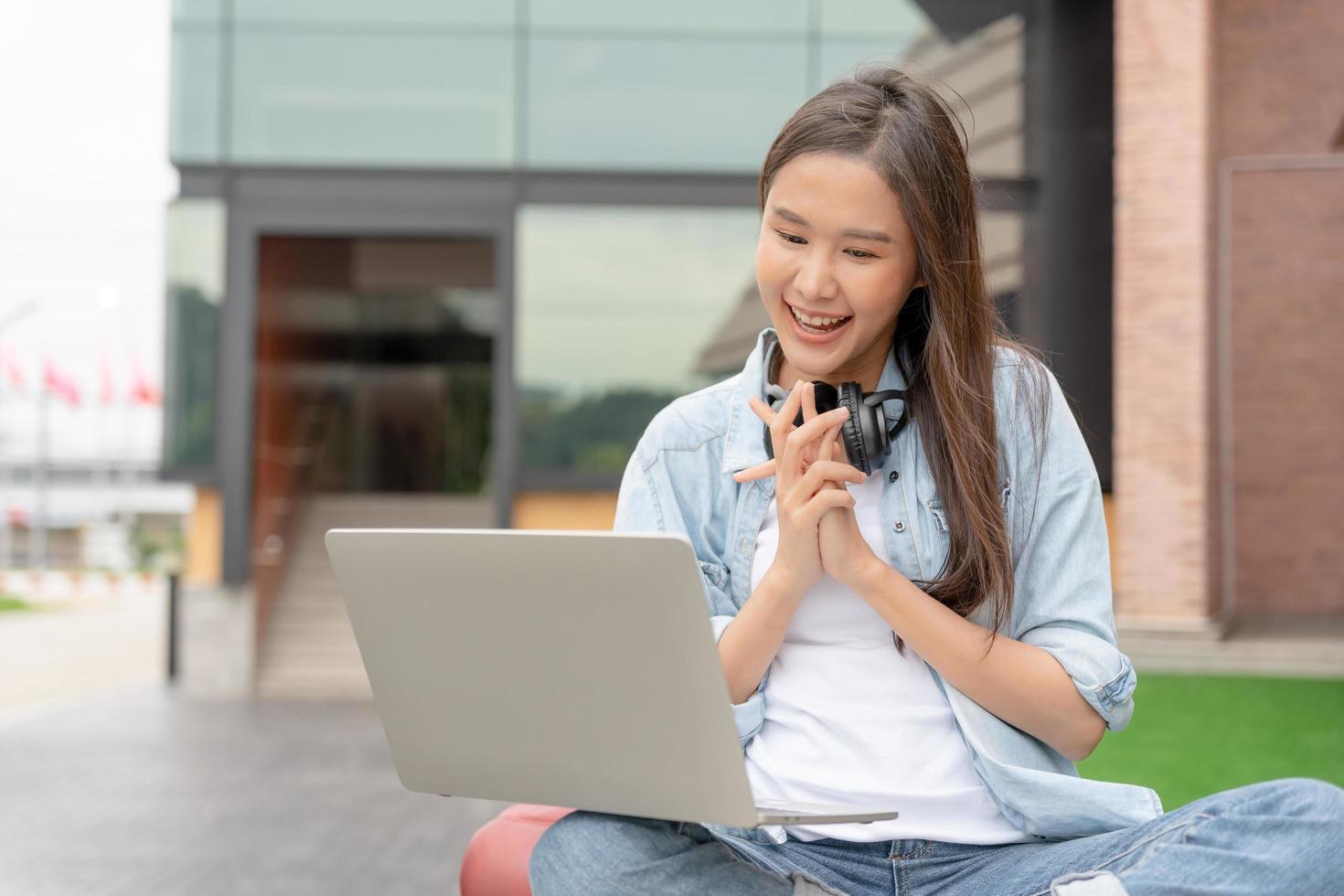 Beautiful Asian woman female student excited checking language test results on laptop. Smile girl happy study online. book in college campus. Portrait female on international Asia University. photo