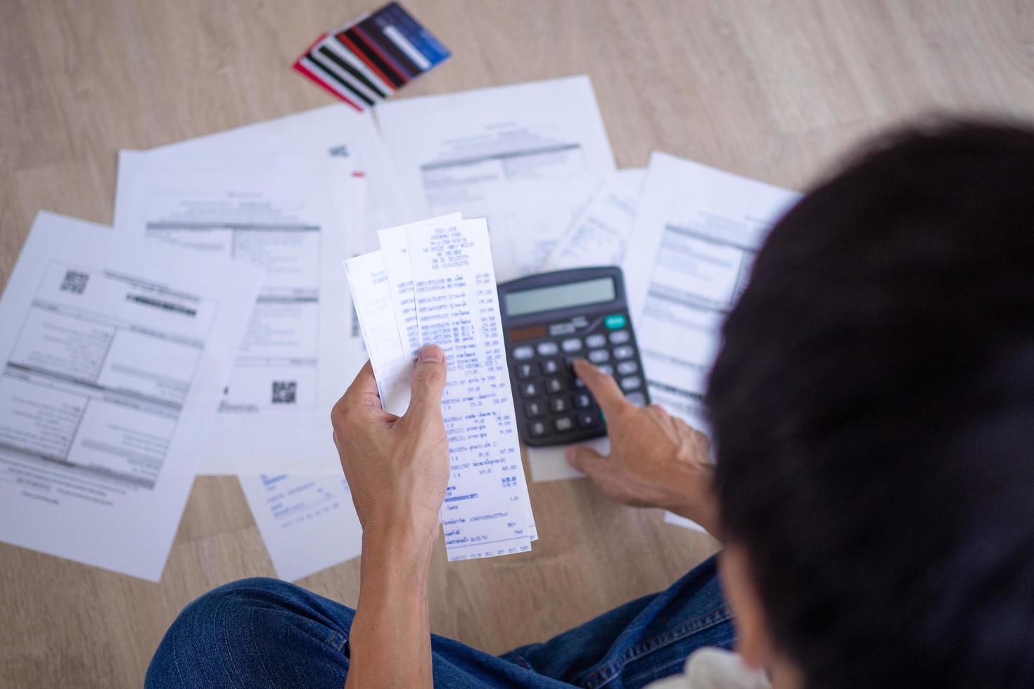 el hombre asiático está estresado por los problemas financieros. con facturas y varias facturas y calculadoras colocadas mientras tiene problemas con los gastos de la casa. concepto de deuda foto