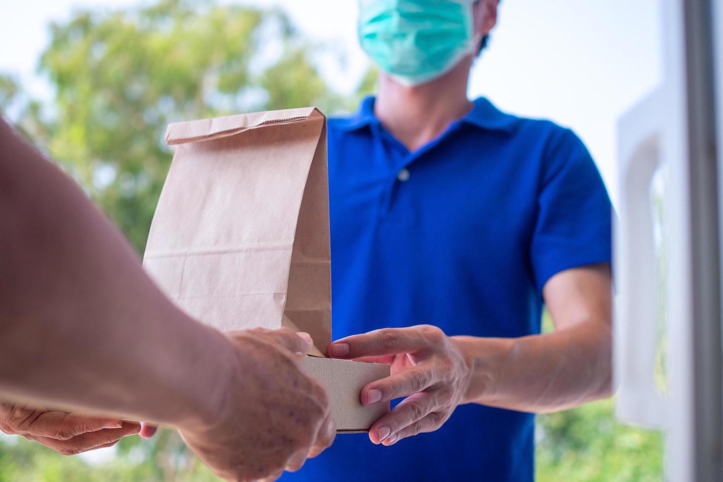 una mujer pidió comida en línea para comer en casa. la persona pide productos o comida en línea, recibe paquetes del repartidor que pone una máscara en la puerta de la casa. foto