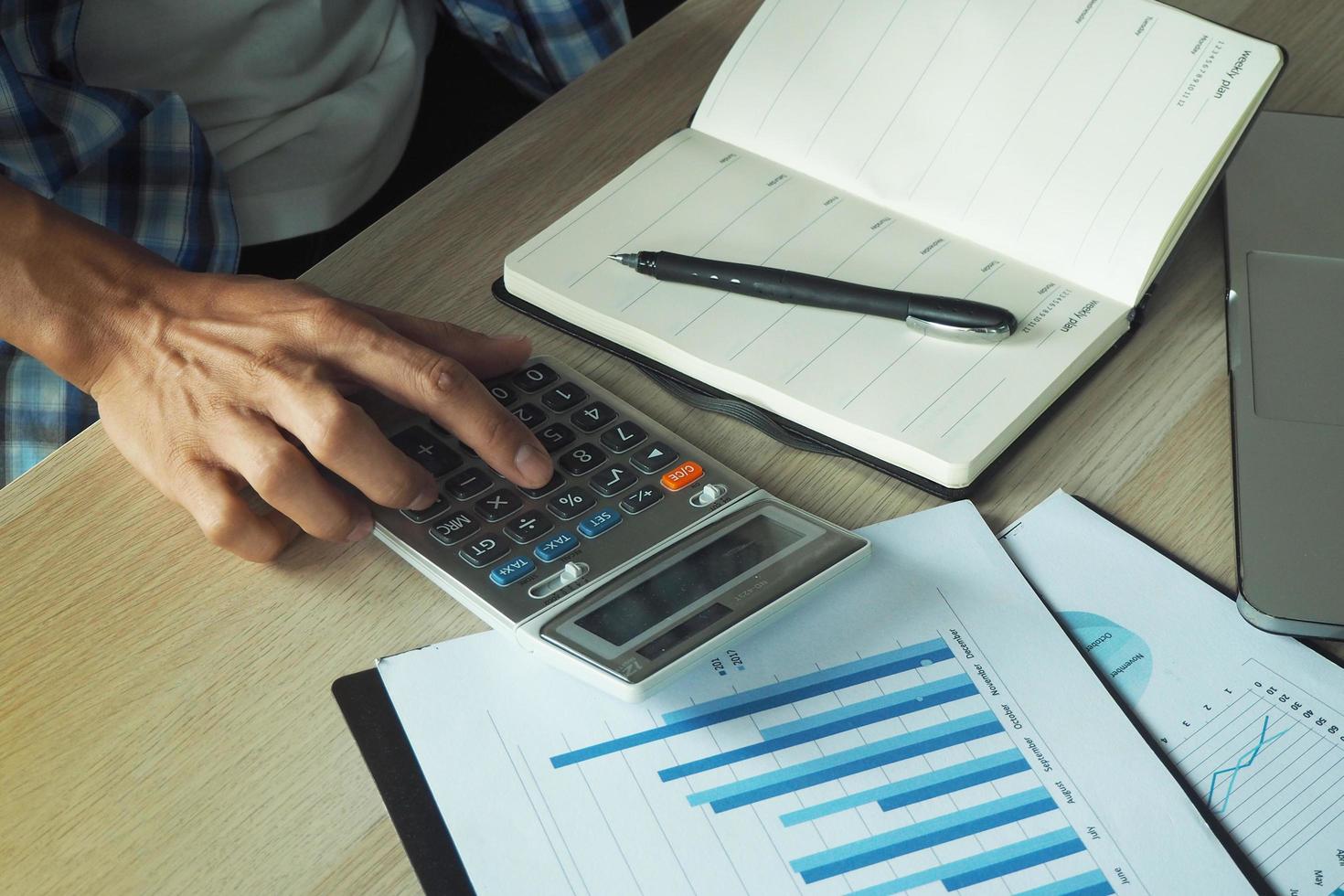 un empleado masculino está usando una calculadora para calcular su trabajo. Tenga un cuaderno y anote la información y la información estadística para ayudar a analizar. foto