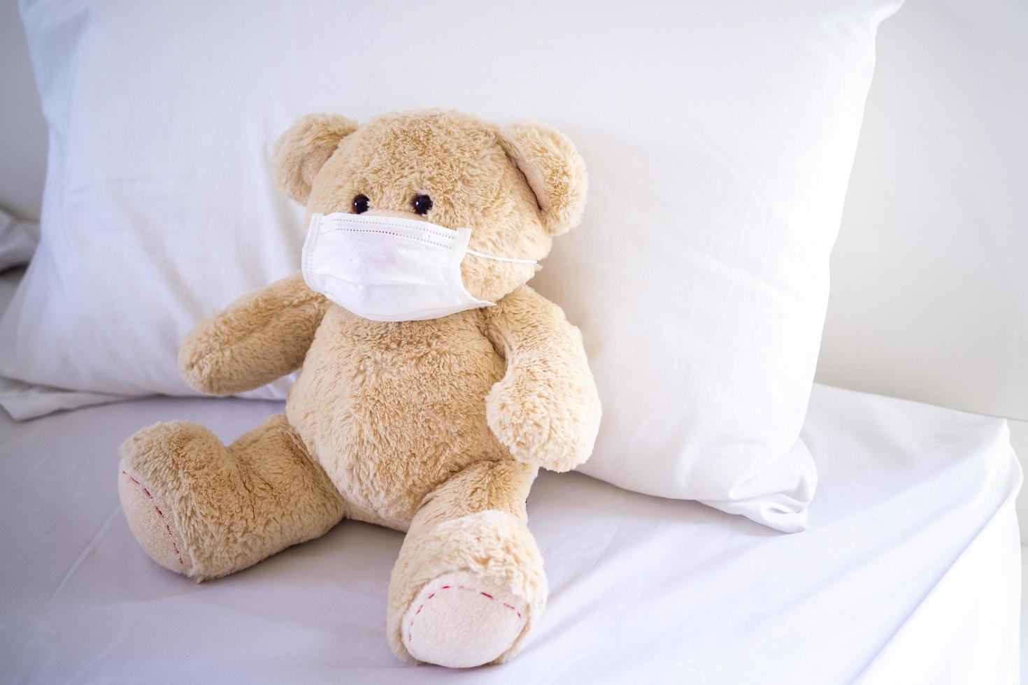 The teddy bear is sitting on a bed wearing a mask to protect against germs and viruses. Hygiene for children concept photo