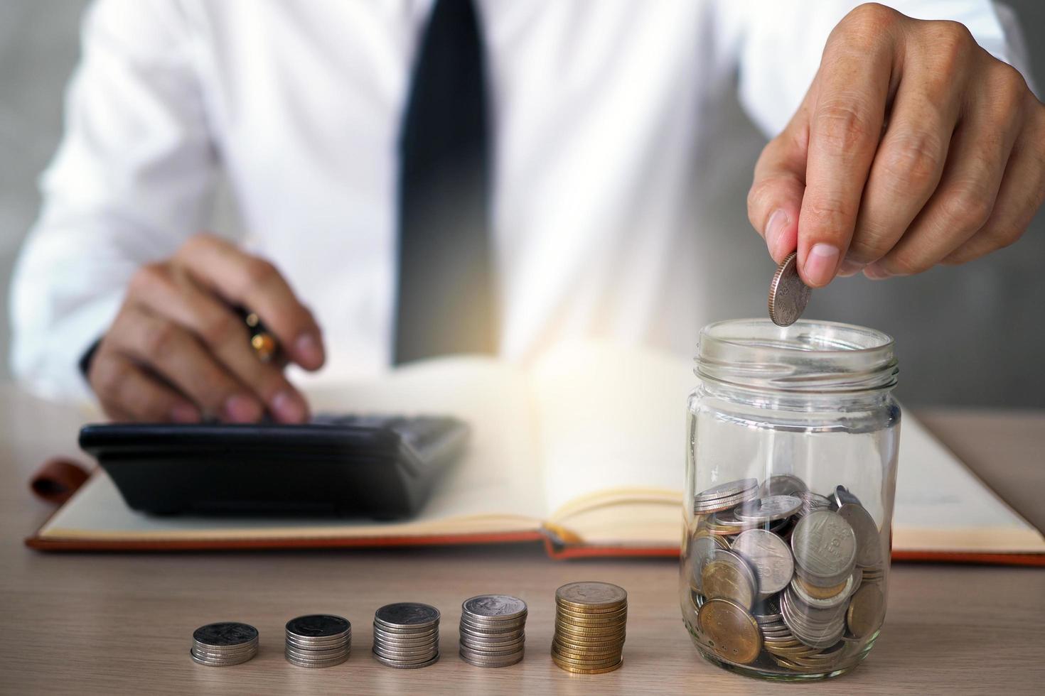 Businessmen calculate income and hold coins in a glass bottle. There are piles of coins around. photo