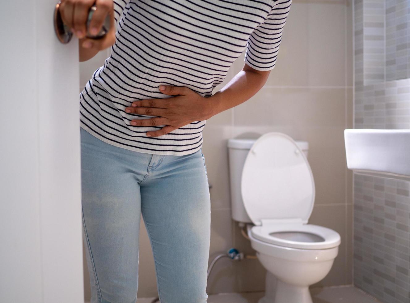 Woman with diarrhea standing in the bathroom, holding her stomach. Severe stomach pain, prepare to sit dung in the bathroom photo