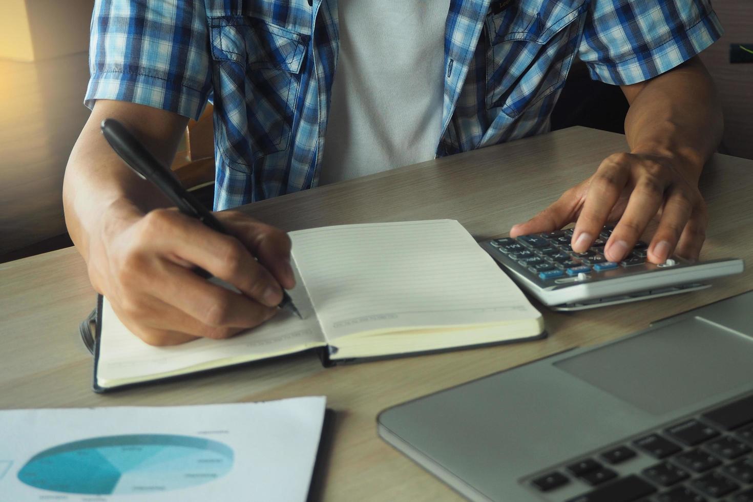 la mano del hombre está escribiendo un resumen de los cálculos de ingresos y gastos de la empresa. el concepto de escritura y contabilidad foto