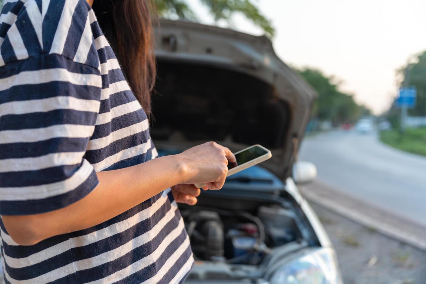 breakdown, broken car, repair. Woman uses mobile phone check insurance premiums through application due to car accident . Find garage to get car fixed during country tour, waiting for help, emergency. photo