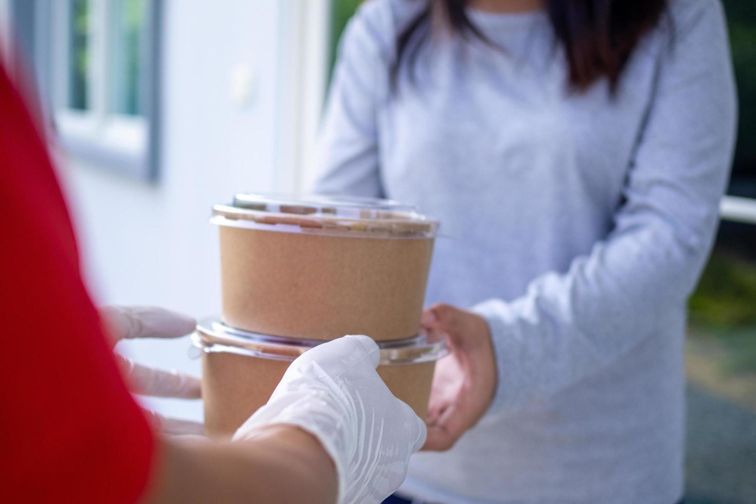 Delivery staff wear gloves for good hygiene, send food boxes to recipients in front of the house. Order food online and fast delivery. photo