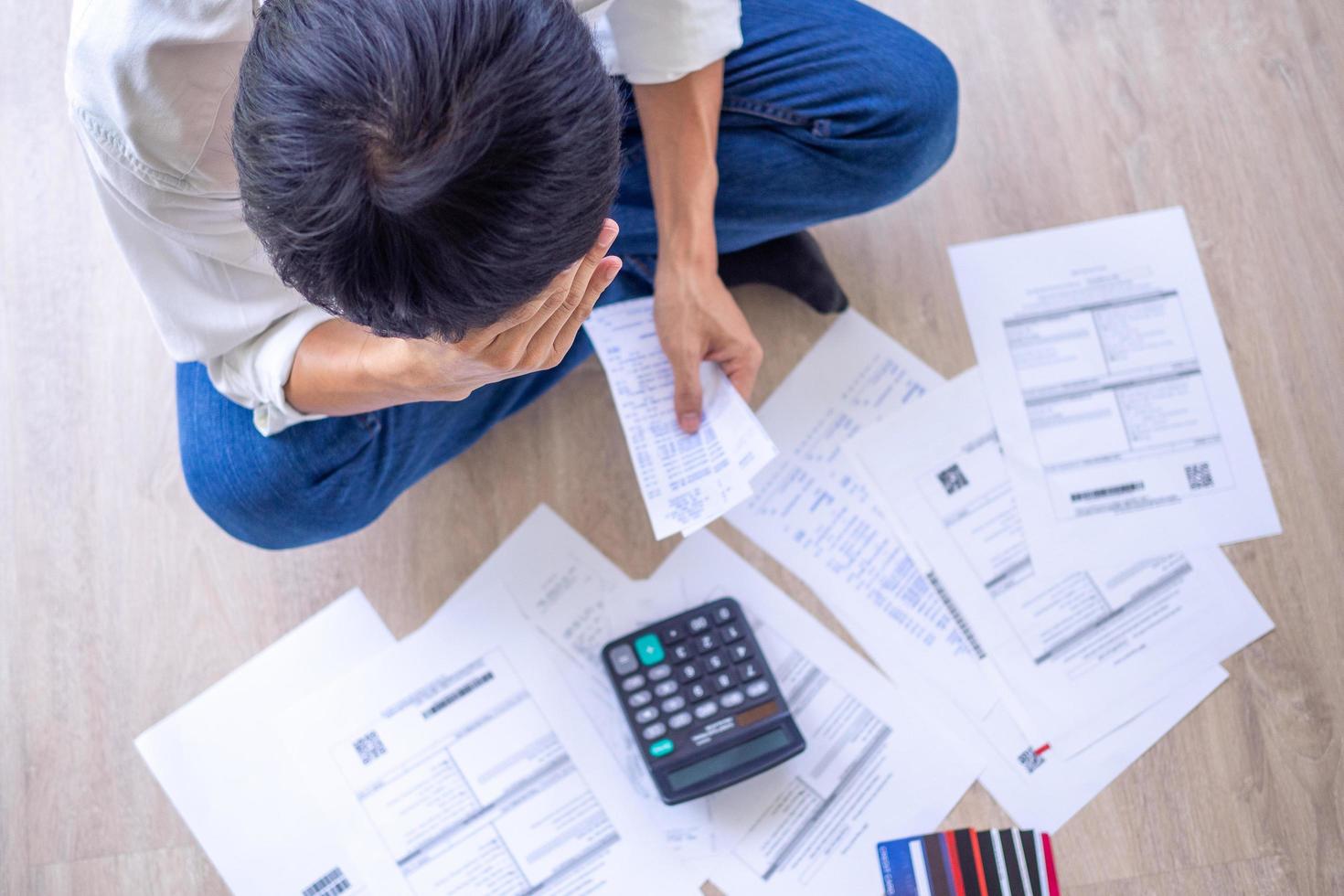 el hombre asiático está estresado por los problemas financieros. con facturas y varias facturas y calculadoras colocadas mientras tiene problemas con los gastos de la casa. concepto de deuda foto