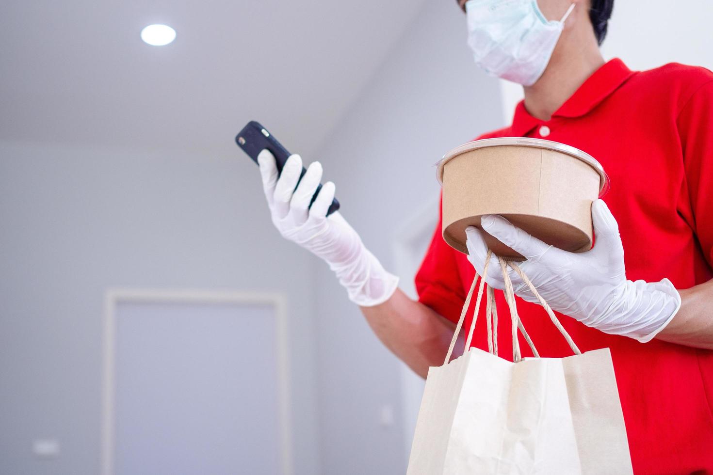 Delivery man holding paper bag and boxes with food. Food delivery to homes or apartments to prevent germs by wearing masks and gloves. photo