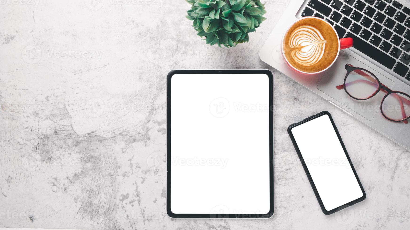 Office desk workplace with blank screen tablet and smart phone, laptop, eyeglass and cup of coffee, Top view flat lay with copy space. photo