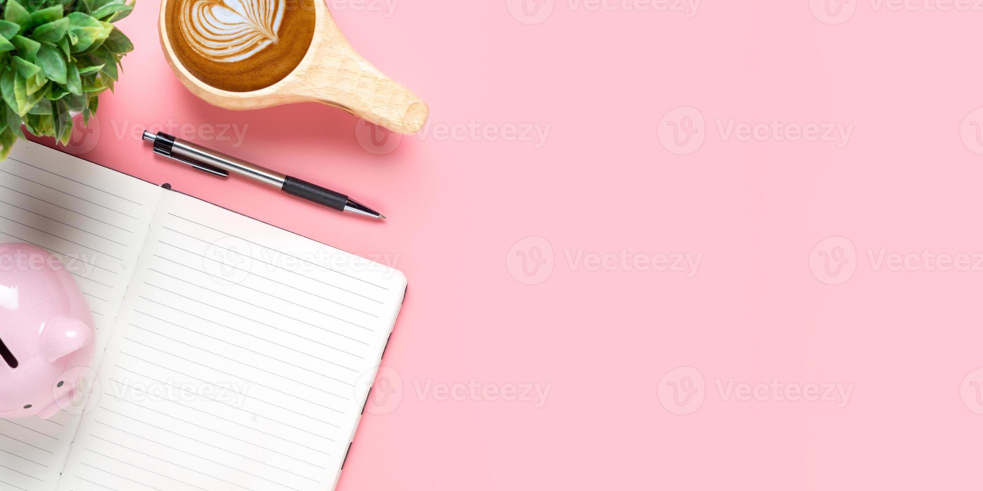 Office desk with Pen, Notebook, Cup of coffee, piggybank on pink background, Top view with copy space, Mock up. photo