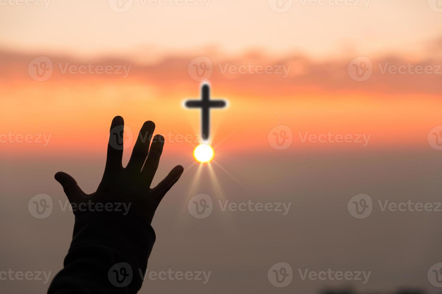 fe del concepto cristiano. la oración espiritual entrega el brillo del sol con un hermoso fondo de puesta de sol borroso. las manos femeninas adoran a dios con amor y fe. silueta de una mujer rezando con una cruz. foto