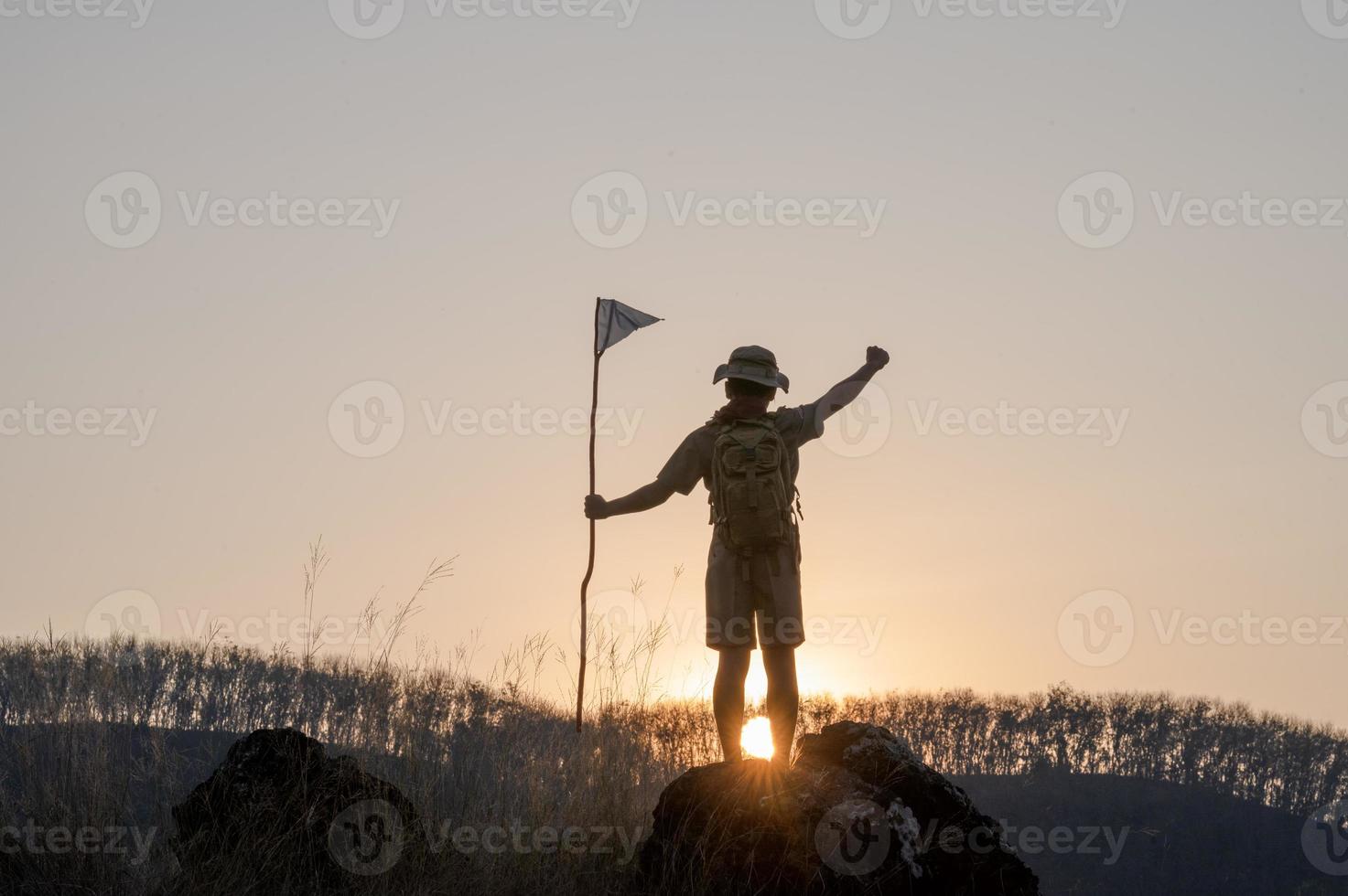 Silhouette of America Boy Scouts holding flag on top of mountain with blue sky and sunlight. It symbolizes the leadership of the Scouts in the trekking that achieves their goals and objectives. photo