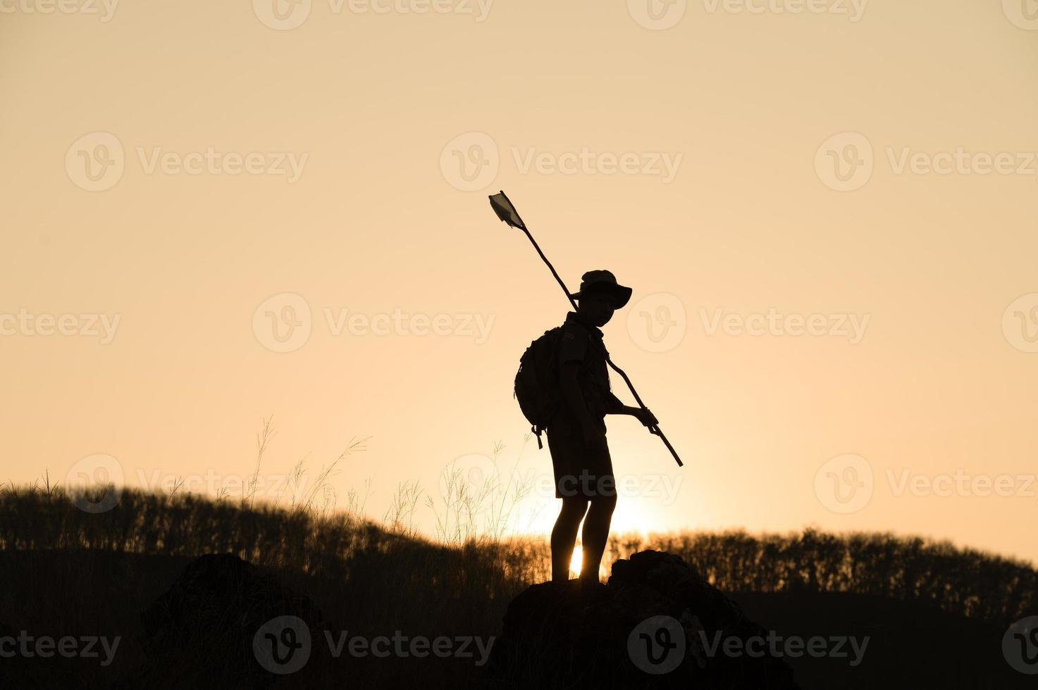 Silhouette of America Boy Scouts holding flag on top of mountain with blue sky and sunlight. It symbolizes the leadership of the Scouts in the trekking that achieves their goals and objectives. photo