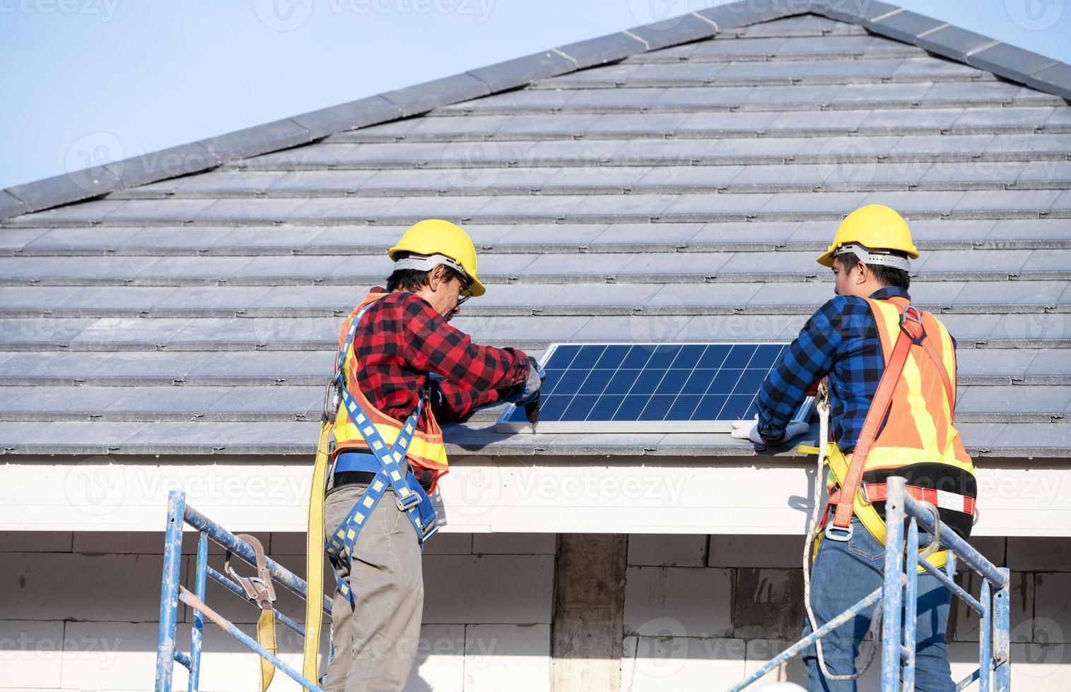 A team of Asian technicians installs solar panels on the roof of a house. Cross-section view of builder in helmet installing solar panel system concept of renewable energy photo