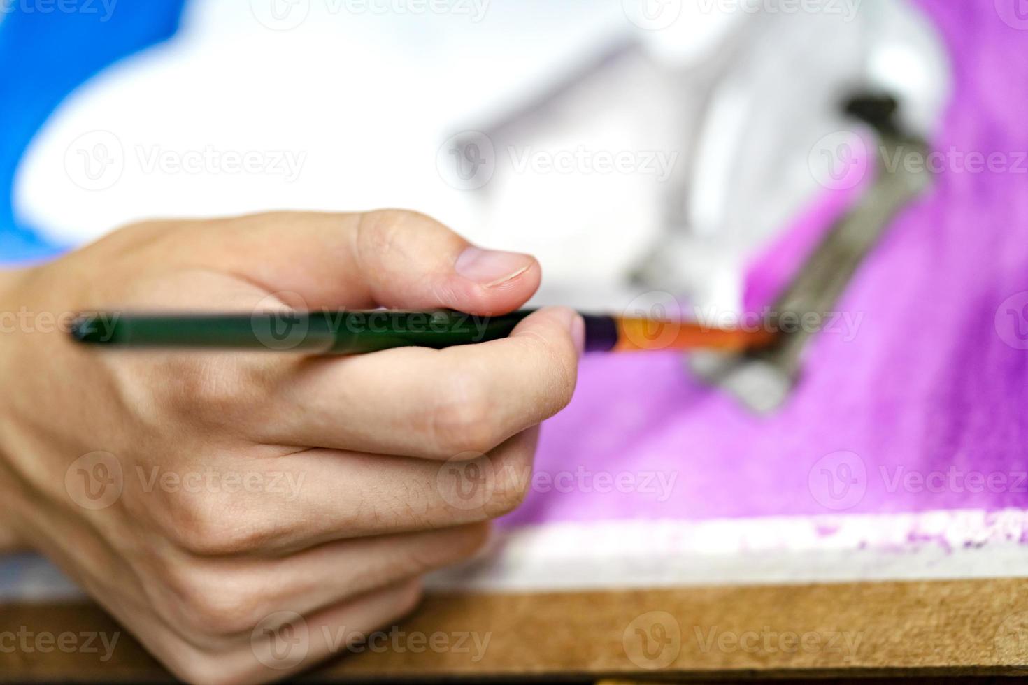 closeup hands holding brush with watercolor paints by artist painting photo