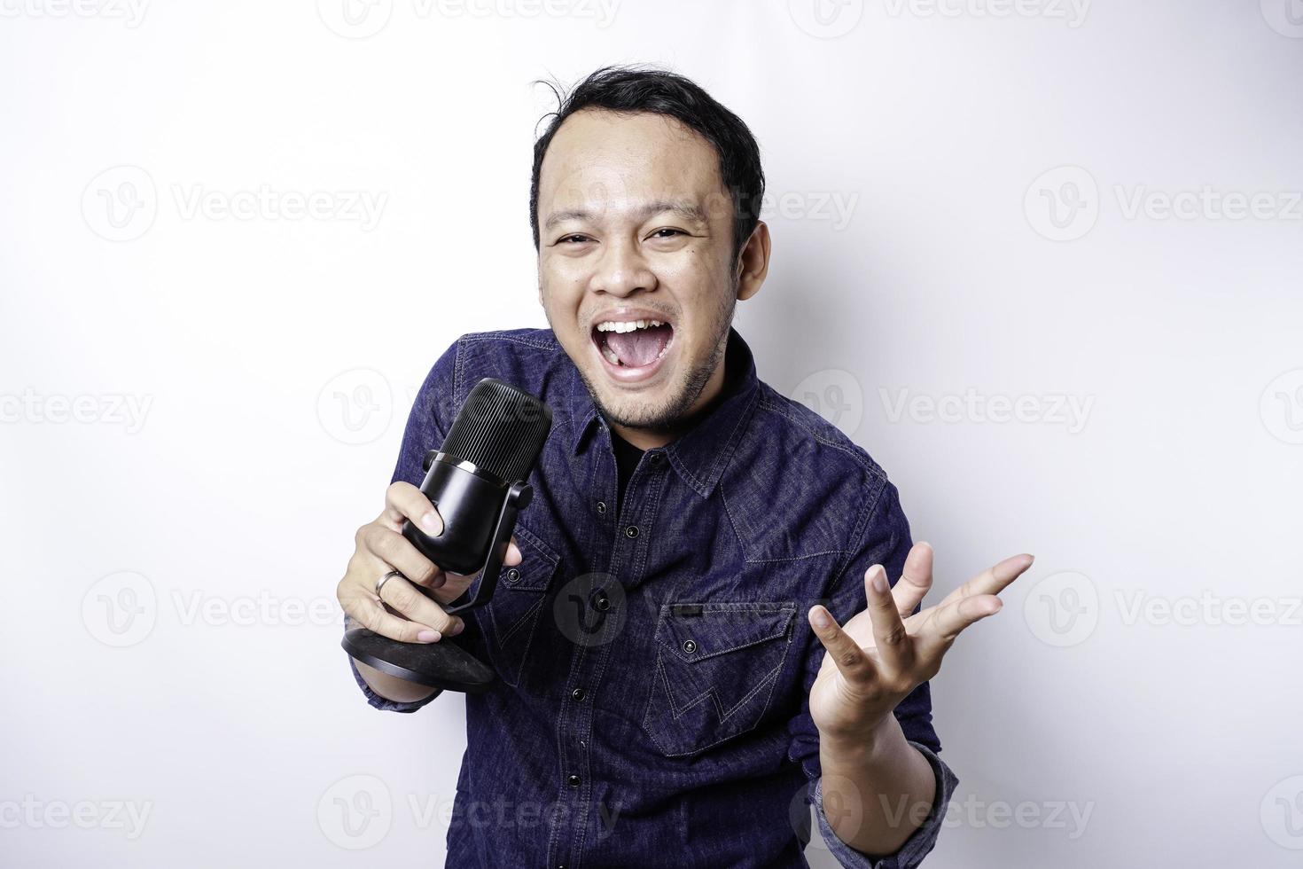 Portrait of carefree Asian man, having fun karaoke, singing in microphone while standing over white background photo
