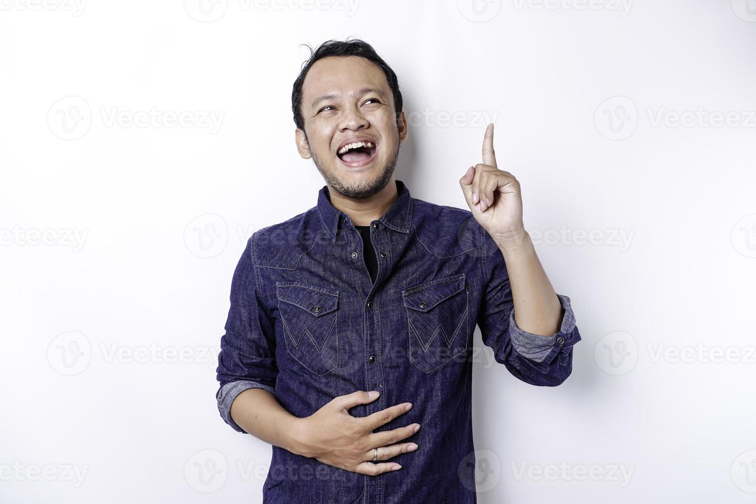 Starving Asian man wearing blue shirt pointing at the copy space on top of him, isolated by white background photo
