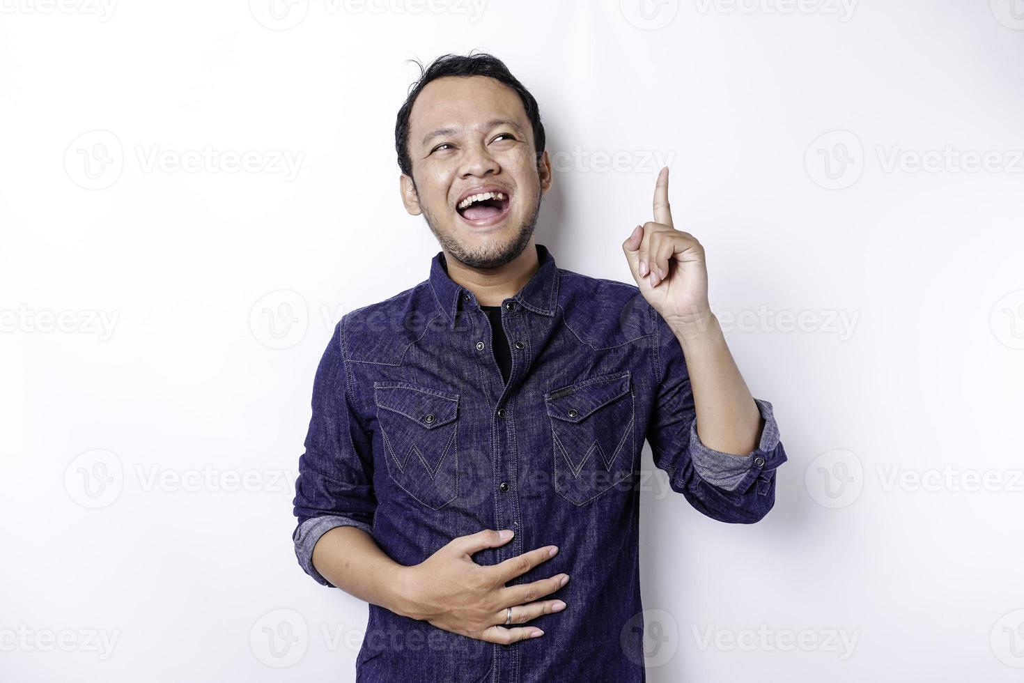 hombre asiático hambriento con pantalones azul apuntando al espacio de copia encima de él, aislado por fondo blanco foto