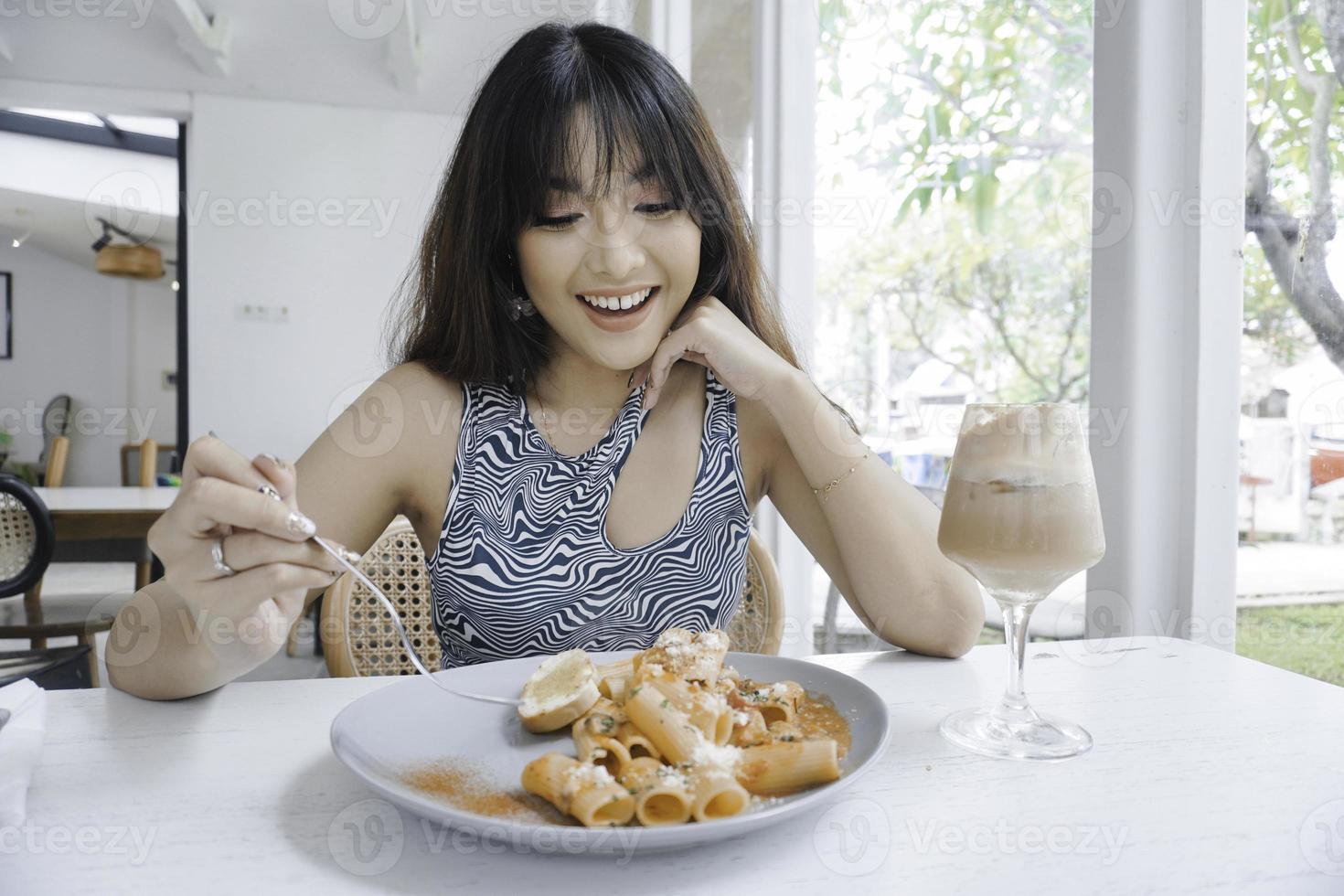 Mujer asiática joven divertida que come la pasta sabrosa en café foto