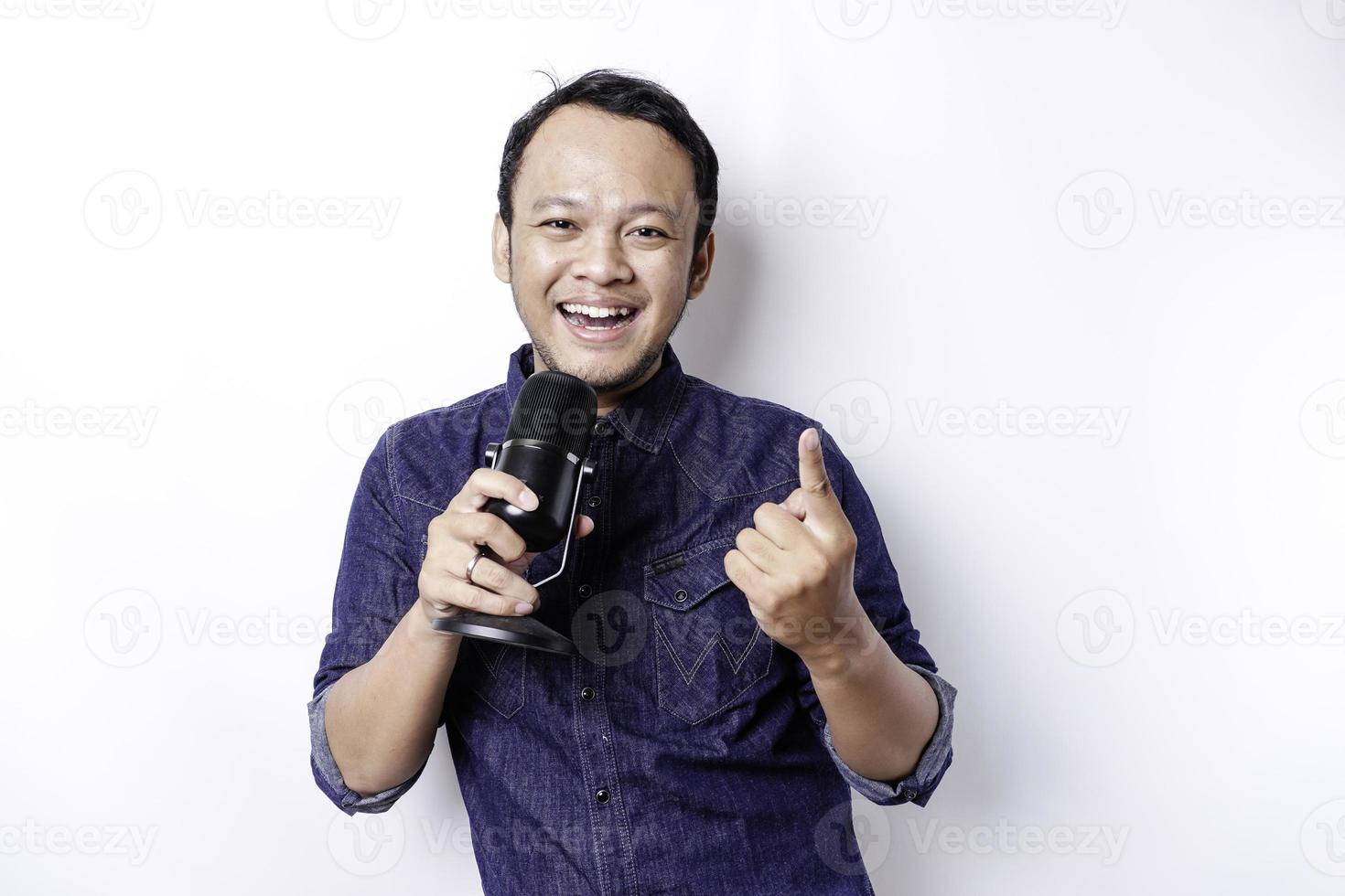 Portrait of carefree Asian man, having fun karaoke, singing in microphone while standing over white background photo