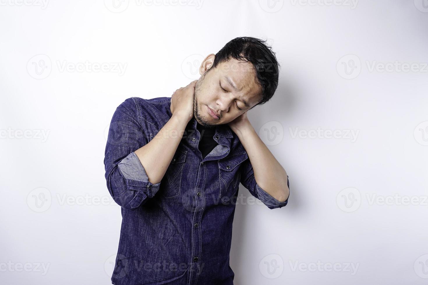 Tired upset young man wears blue shirt suffering from pain, muscle spasm at workplace. Fatigue, deadline, pain and incorrect posture photo