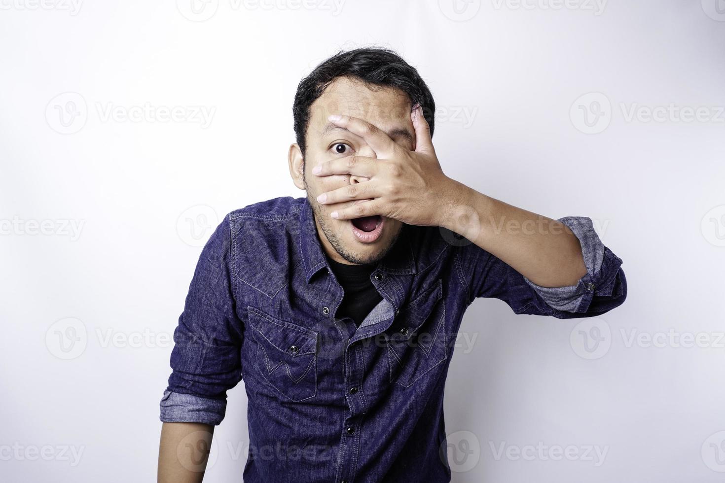 gracioso hombre asiático que mira a escondidas con camisa azul aislado de fondo blanco. foto