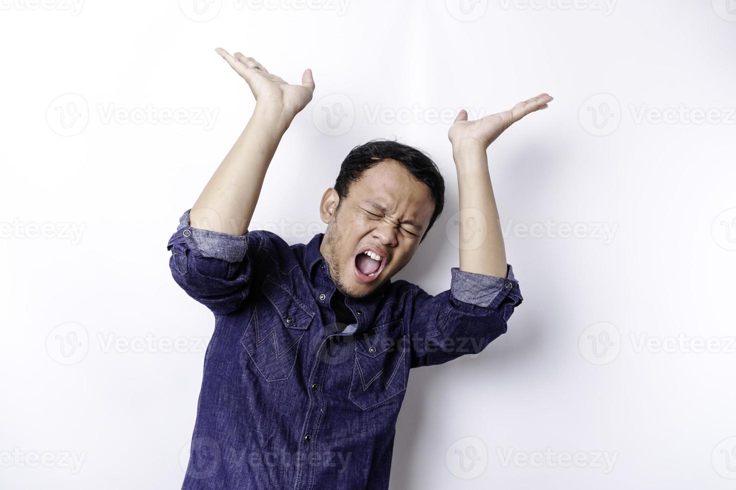 hombre asiático conmocionado con camisa azul apuntando al espacio de copia encima de él, aislado por fondo blanco foto