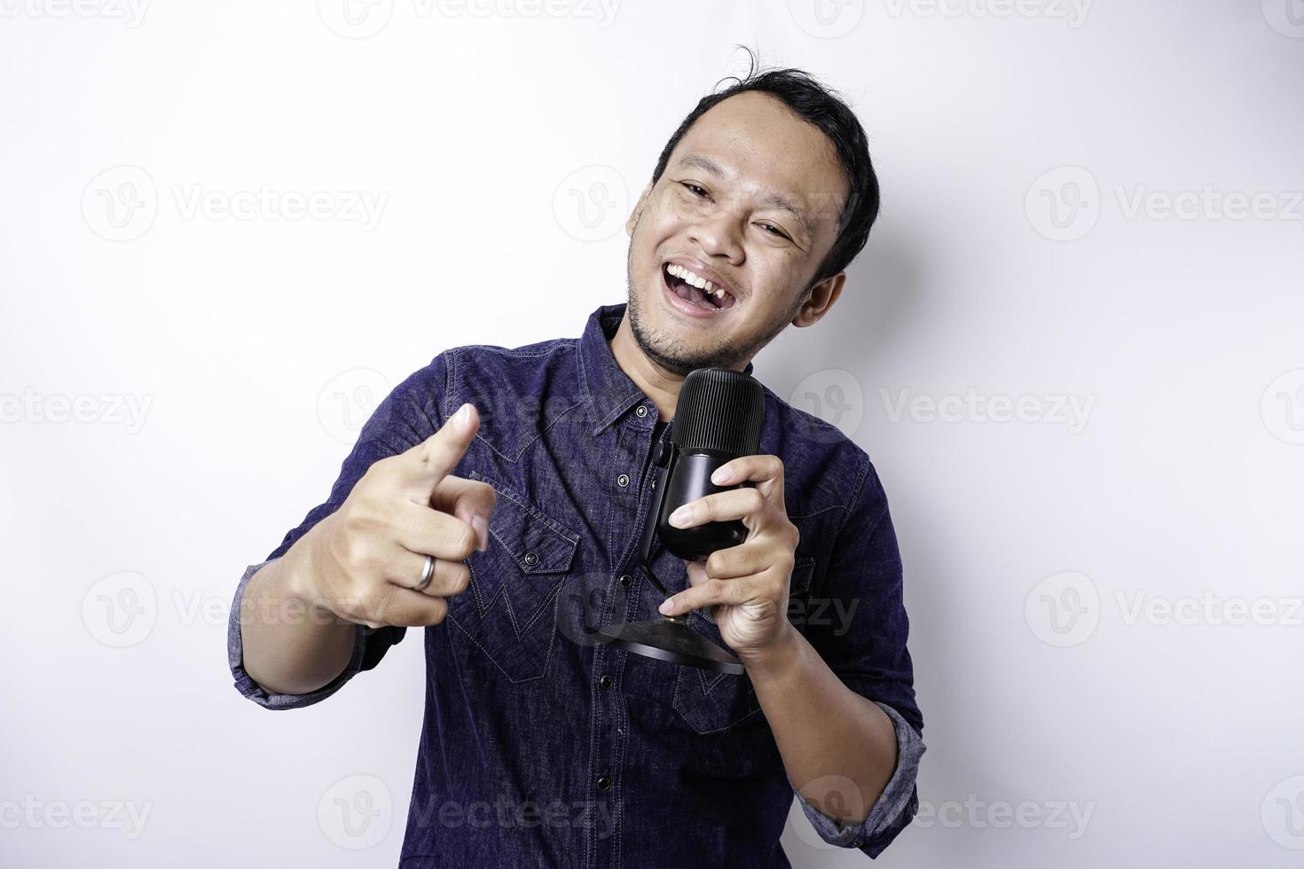 Portrait of carefree Asian man, having fun karaoke, singing in microphone while standing over white background photo