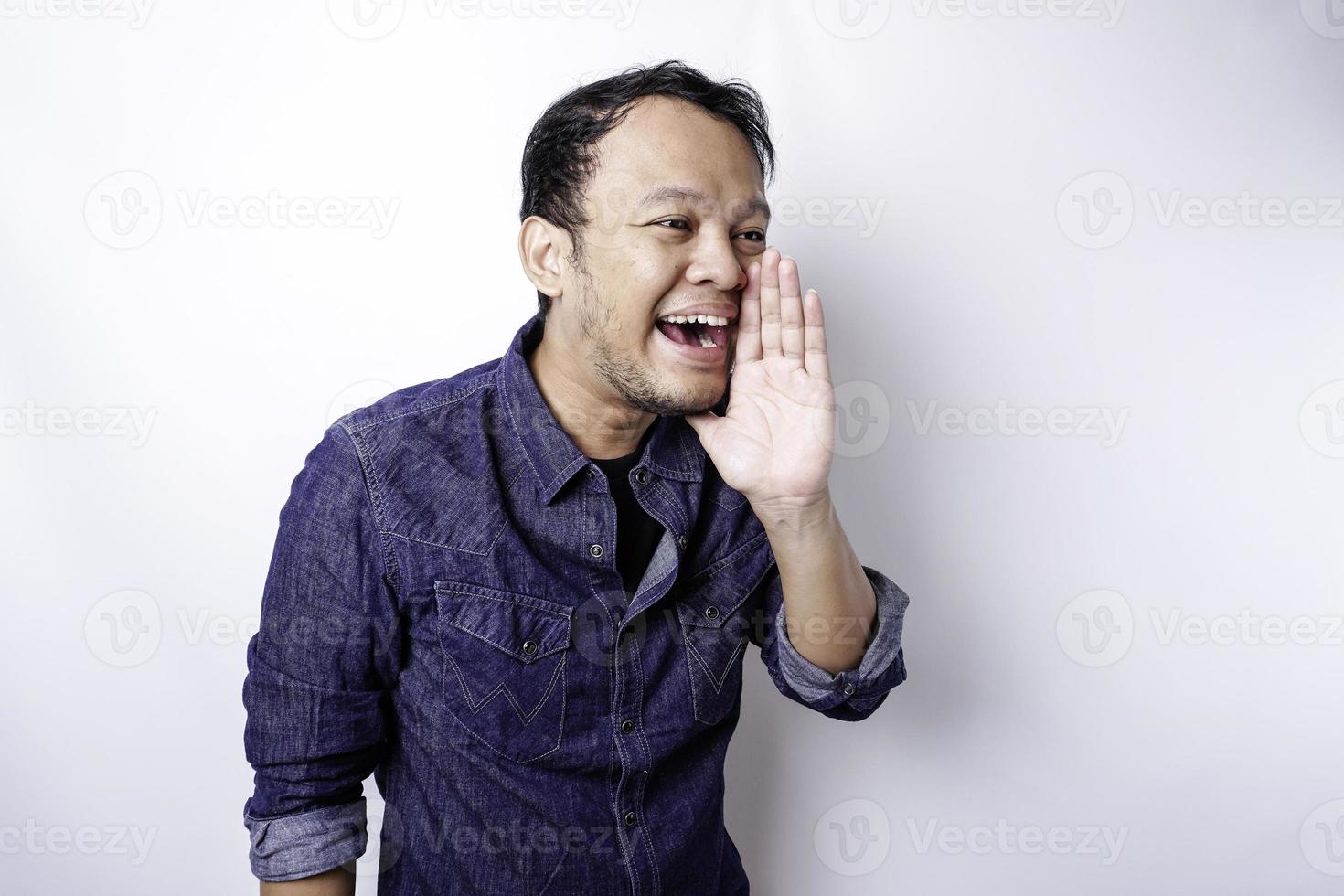 Young handsome man wearing a blue shirt shouting and screaming loud with a hand on his mouth. communication concept. photo