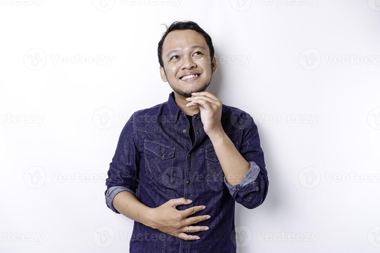 un hombre asiático tiene hambre y se toca el vientre mientras mira a un lado pensando qué comer, aislado de fondo blanco foto