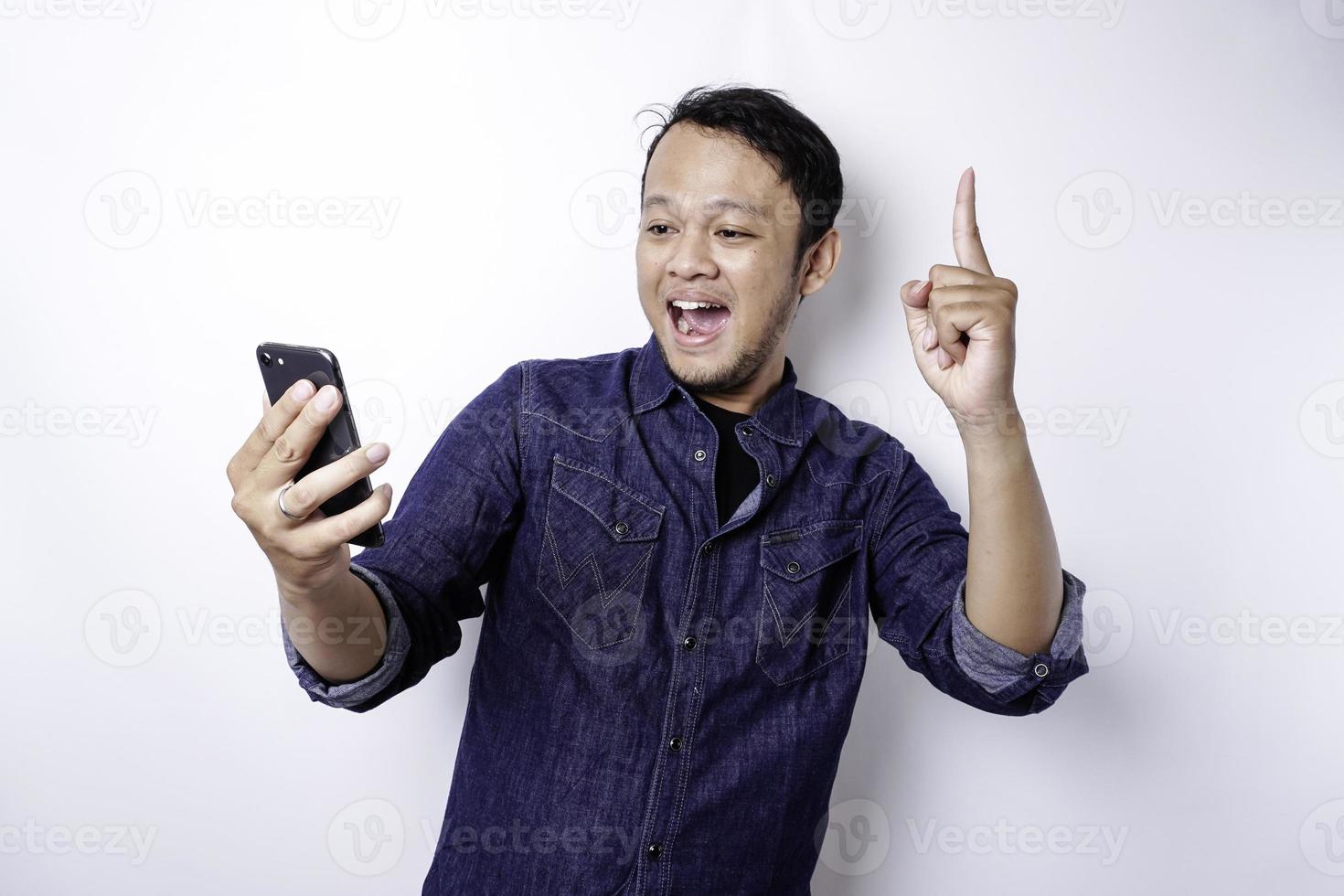 A portrait of a happy Asian man wearing a blue shirt and holding her phone, isolated by white background photo