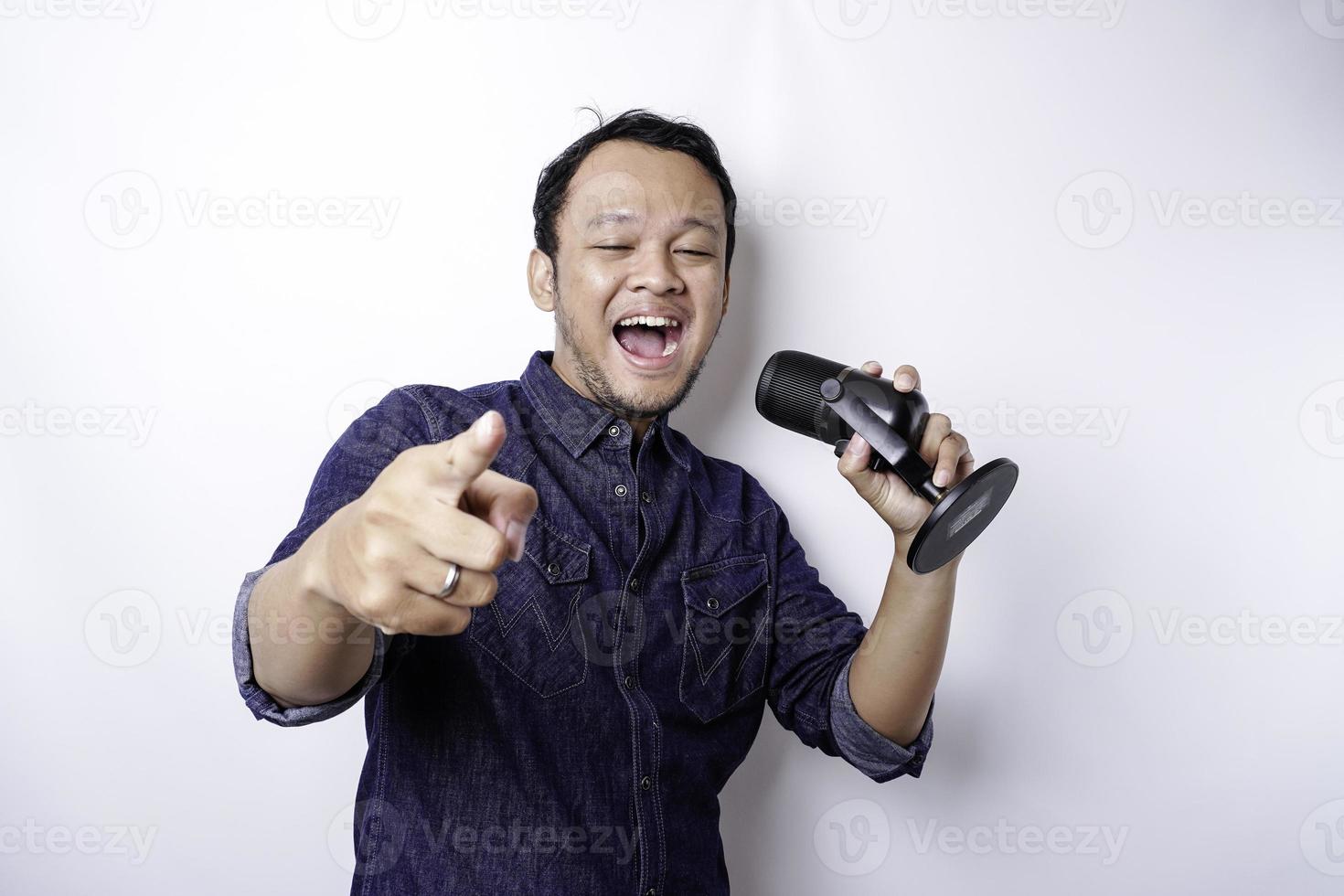 Portrait of carefree Asian man, having fun karaoke, singing in microphone while standing over white background photo