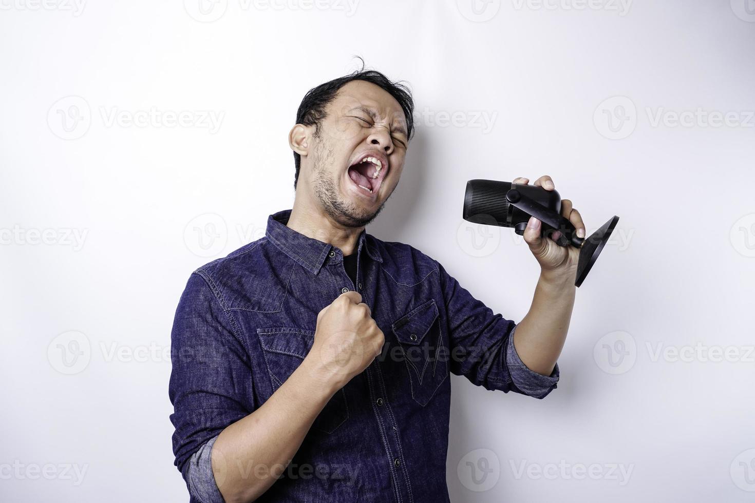 Portrait of carefree Asian man, having fun karaoke, singing in microphone while standing over white background photo