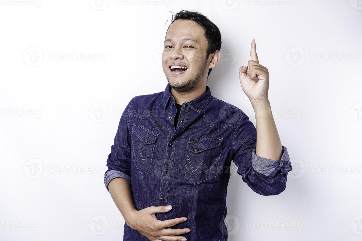 Starving Asian man wearing blue shirt pointing at the copy space on top of him, isolated by white background photo
