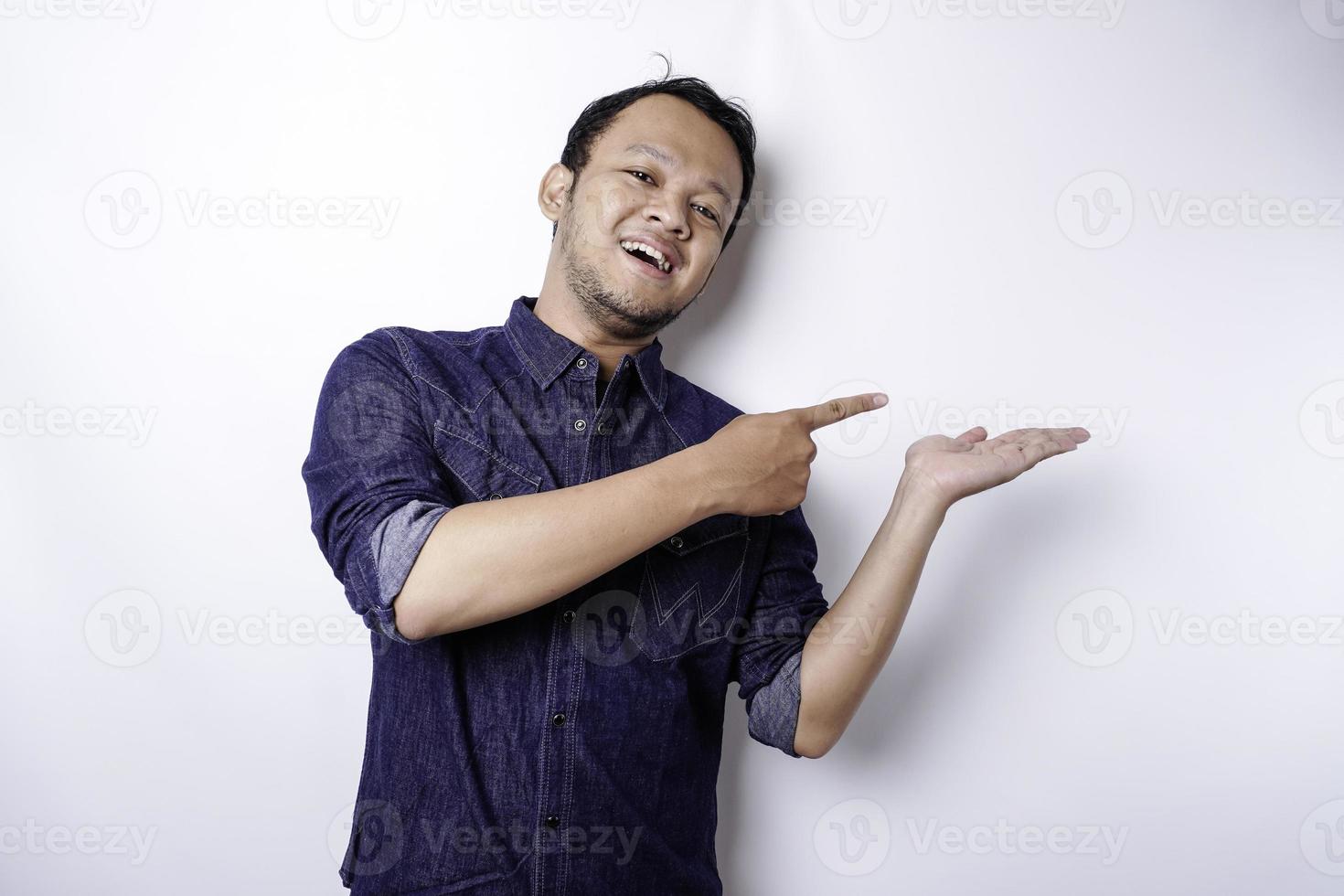 Excited Asian man wearing blue shirt pointing at the copy space beside him, isolated by white background photo