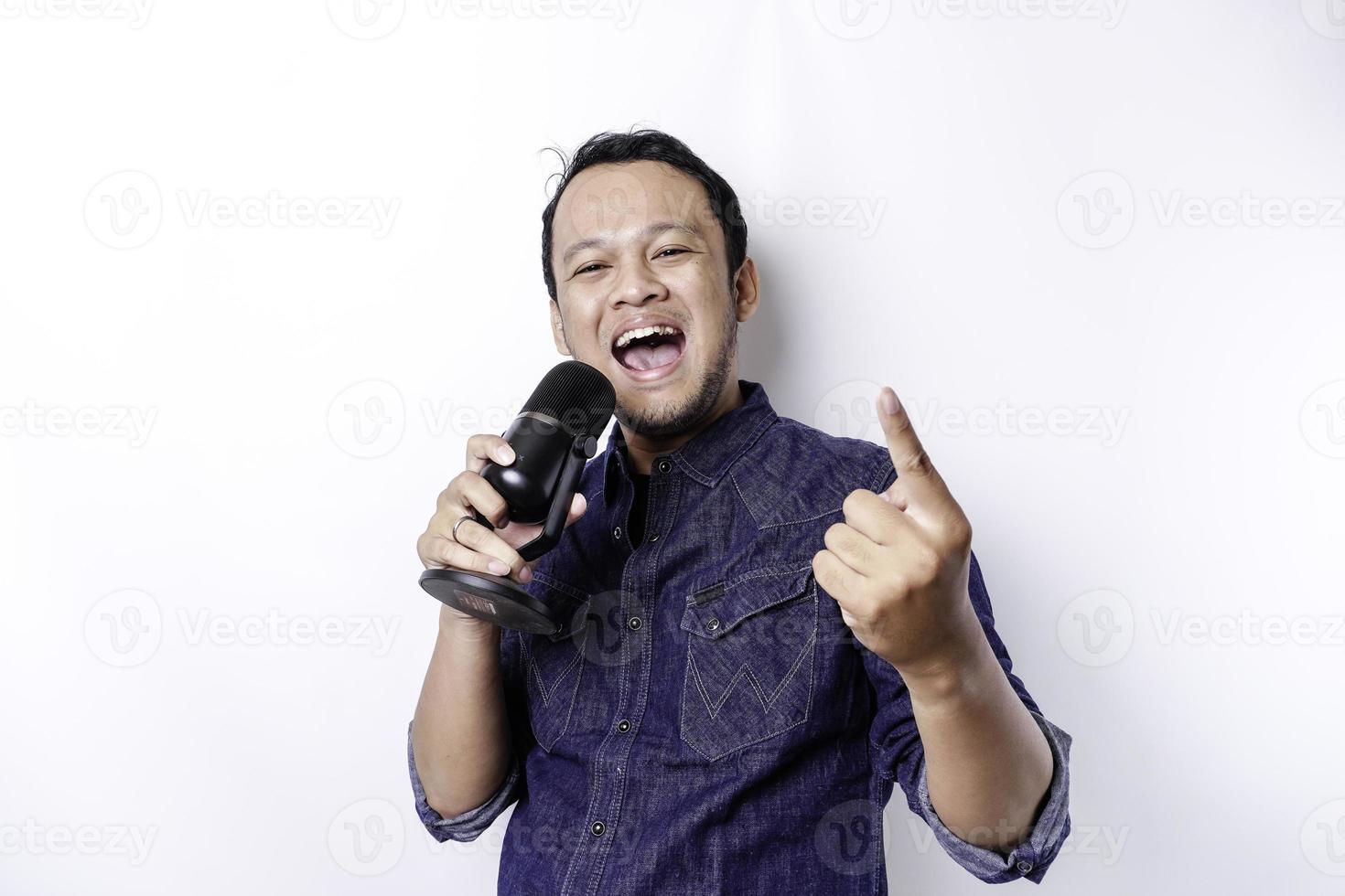 Portrait of carefree Asian man, having fun karaoke, singing in microphone while standing over white background photo