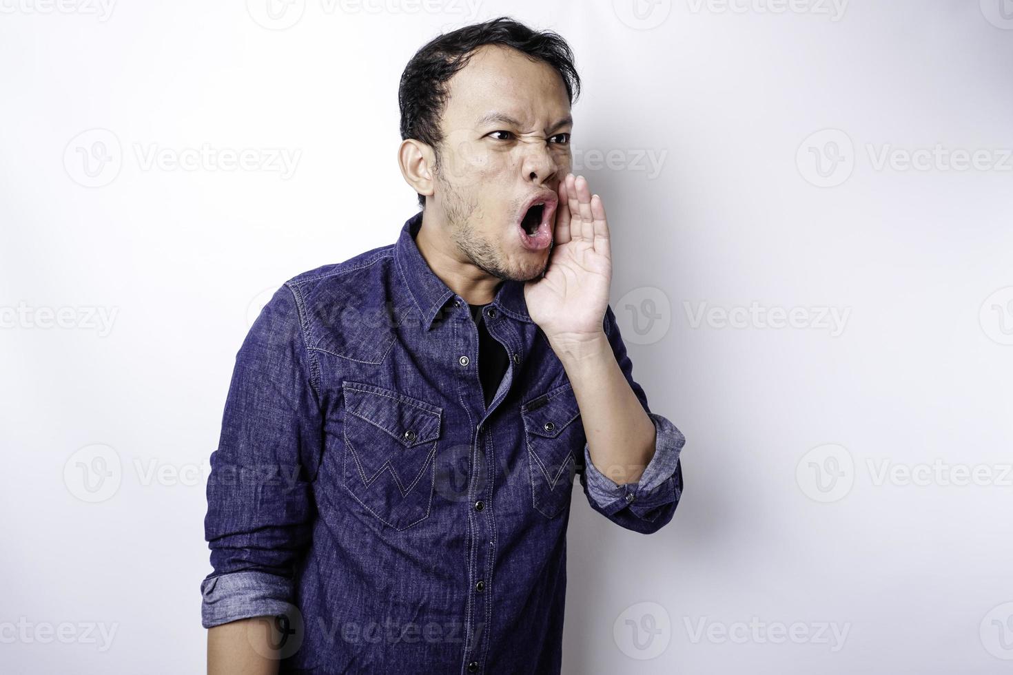 Young handsome man wearing a blue shirt shouting and screaming loud with a hand on his mouth. communication concept. photo