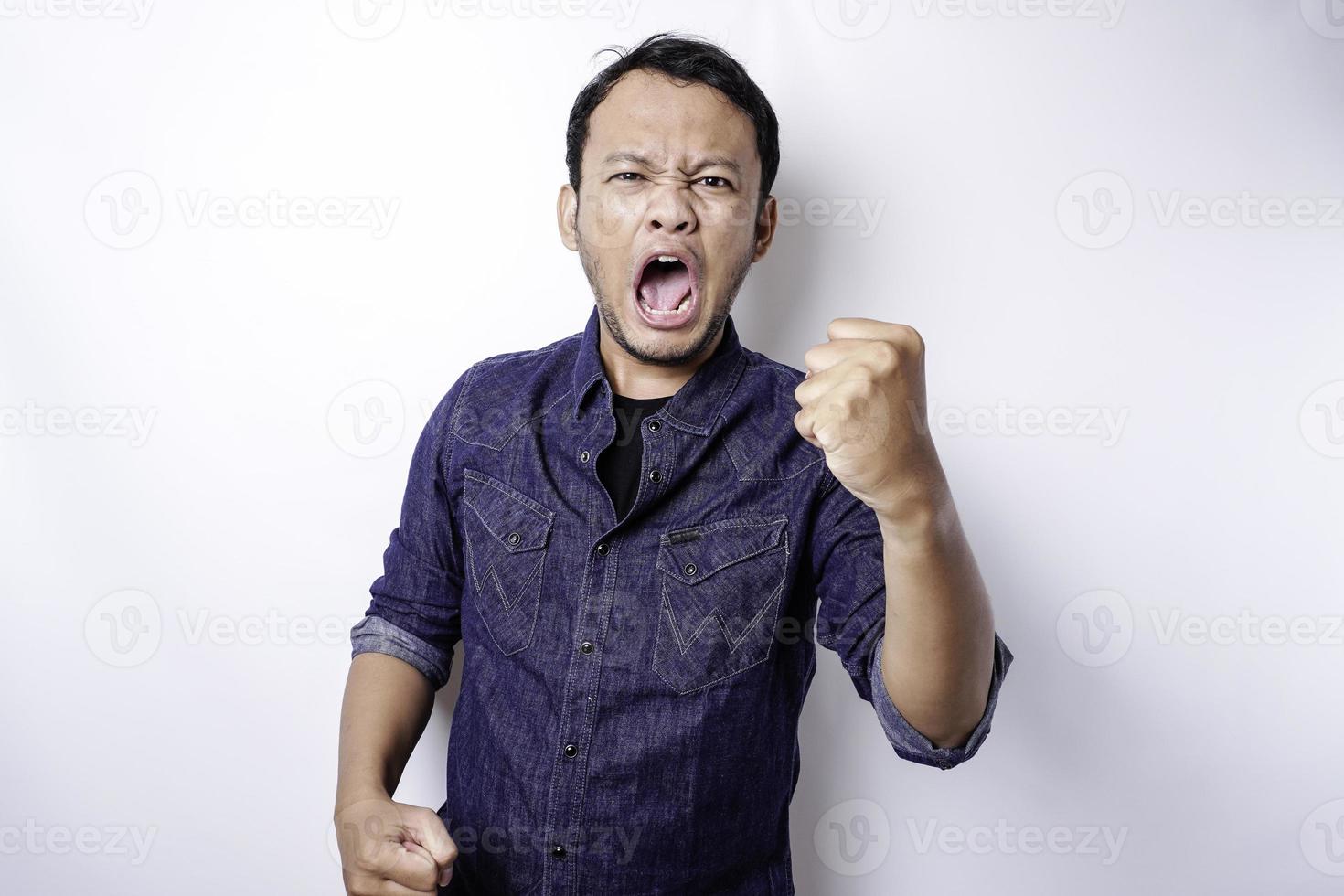 The angry and mad face of Asian man in blue shirt isolated white background. photo