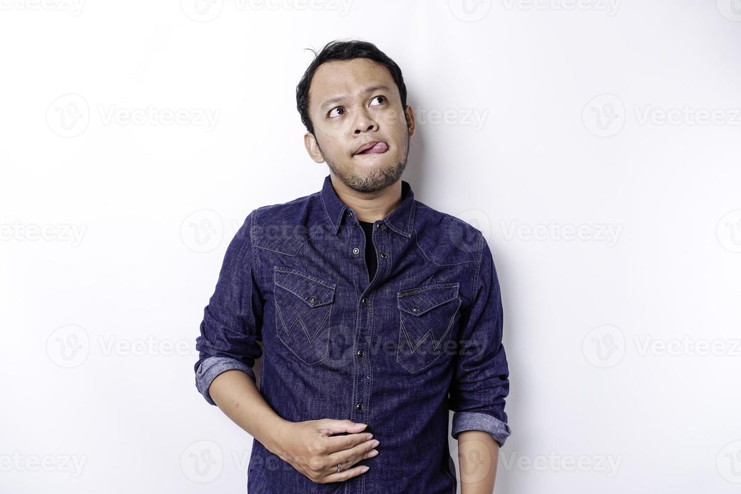 un hombre asiático tiene hambre y se toca el vientre mientras mira a un lado pensando qué comer, aislado de fondo blanco foto